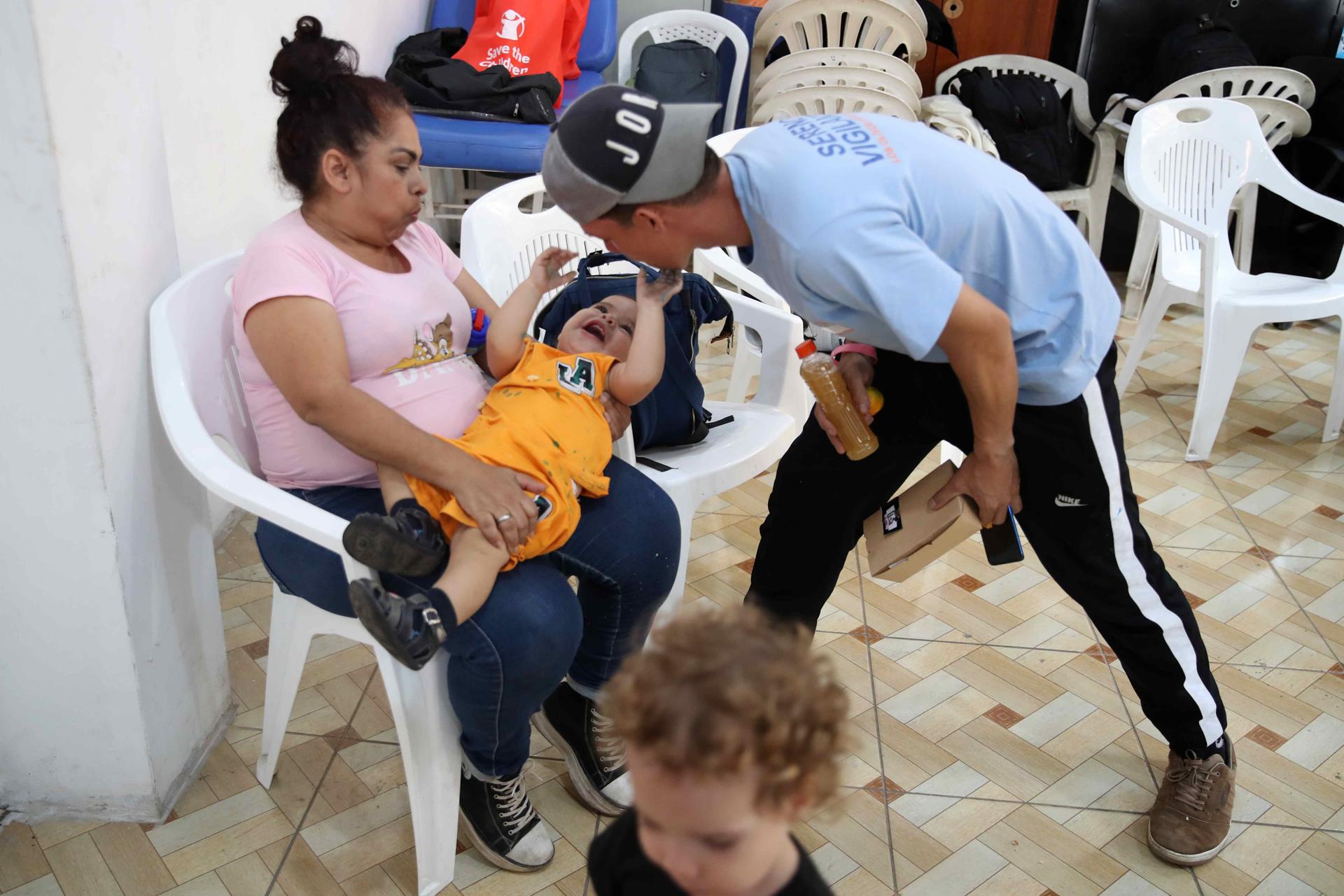 AME5805. LIMA (PERÚ), 08/05/2025.- Fotografía del 28 de abril de 2025 de dos personas jugando con un niño en un centro parroquial en Lima (Perú). Desde una bulliciosa sala con niños que corretean en un centro parroquial de la zona norte de Lima, un grupo de madres venezolanas conversan sobre el alivio que fue para sus familias un proyecto de Save the Children financiado por Usaid, que aportaba tres mensualidades para asegurar su seguridad alimentaria y que se detuvo de forma súbita. EFE/ Paolo Aguilar
