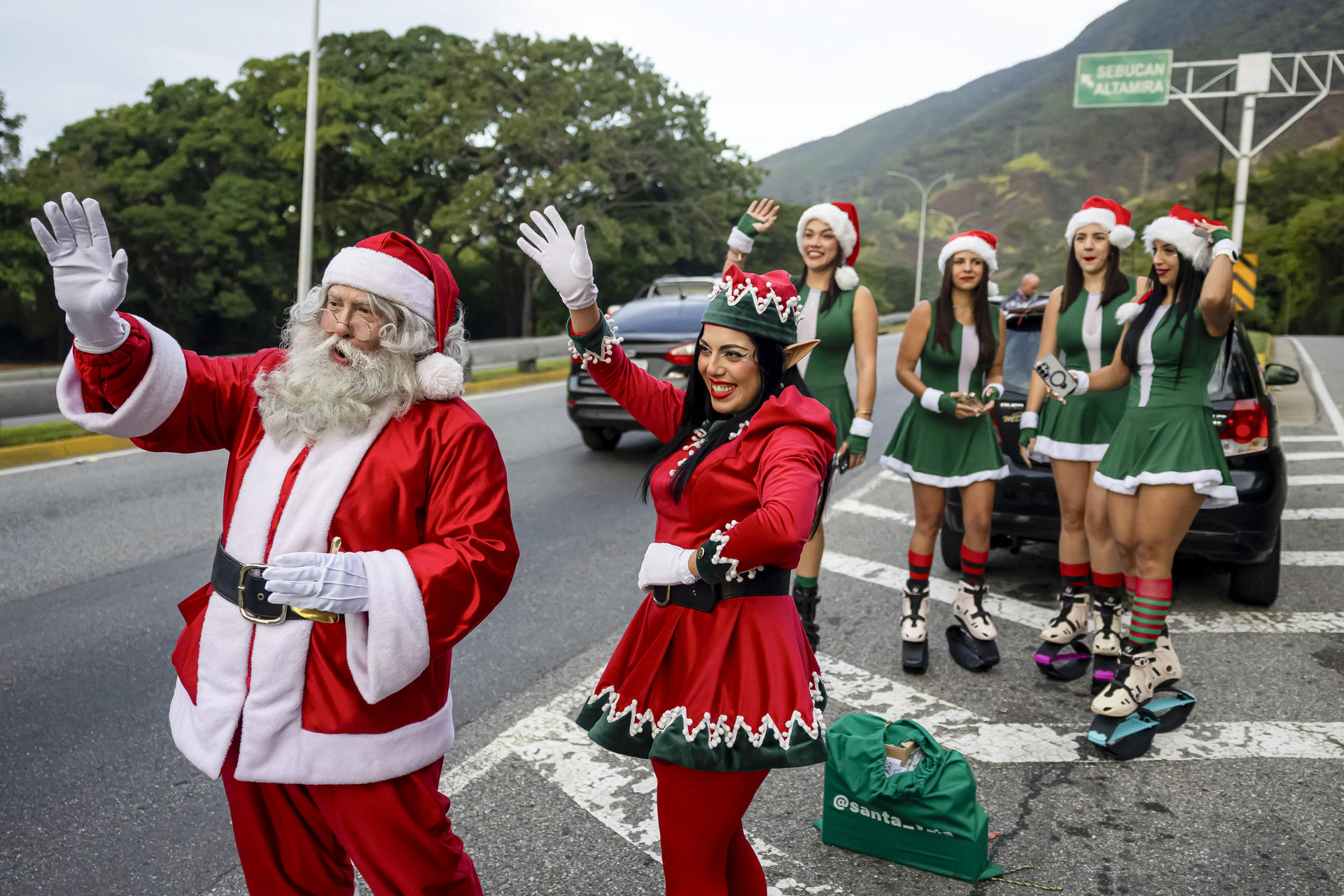 AME4636. CARACAS (VENEZUELA), 01/12/2025.- Personas disfrazadas de personajes alusivos a la navidad saludan a personas que transitan por una autopista este lunes, en Caracas (Venezuela). EFE/ Miguel Gutiérrez
