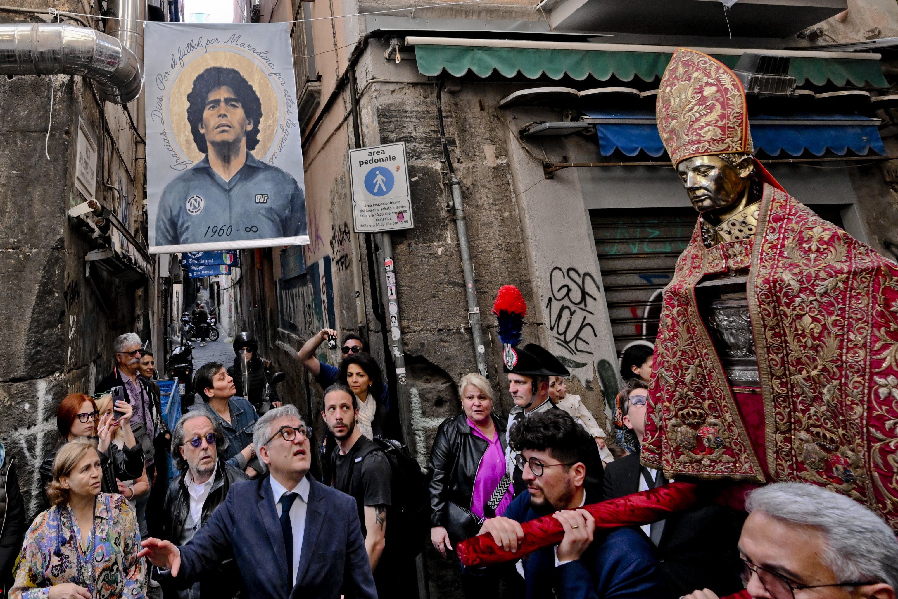 Naples (Italy), 06/05/2023.- People parade with a bust of San Gennaro near a photo of late soccer great Diego Maradona at the historic center of Naples, Italy, 06 May 2023. Faithful usually gather three times a year to witness the liquefaction of the otherwise coagulated blood of San Gennaro the patron saint of Naples. This year the procession was not only followed by the many faithful, who accompanied San Gennaro from the Duomo to the church of Santa Chiara, but also by the hundreds of tourists who flock to the capital of Campania. The parade took place under hundreds of blue flags and banners that have adorned the streets of Naples to celebrate after Napoli clinched their third-ever Serie A league title. (Italia, Nápoles) EFE/EPA/CIRO FUSCO