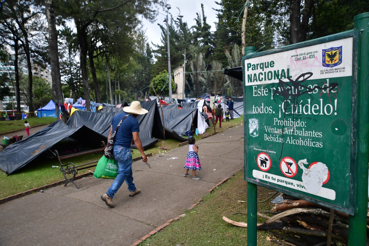 Un hombre y una niña caminan hacia un parque nacional lleno de cambuches y carpas. Los emberas chamís aceptaron salir del parque, pero los embera katios se han declarado en minga permanente hasta que se extiendan las ayudas.