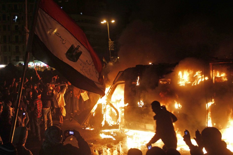 Manifestantes egipcios se paran frente a un vehículo de las fuerzas de seguridad en llamas, mientras los disturbios continúan en el centro de El Cairo. / EFE