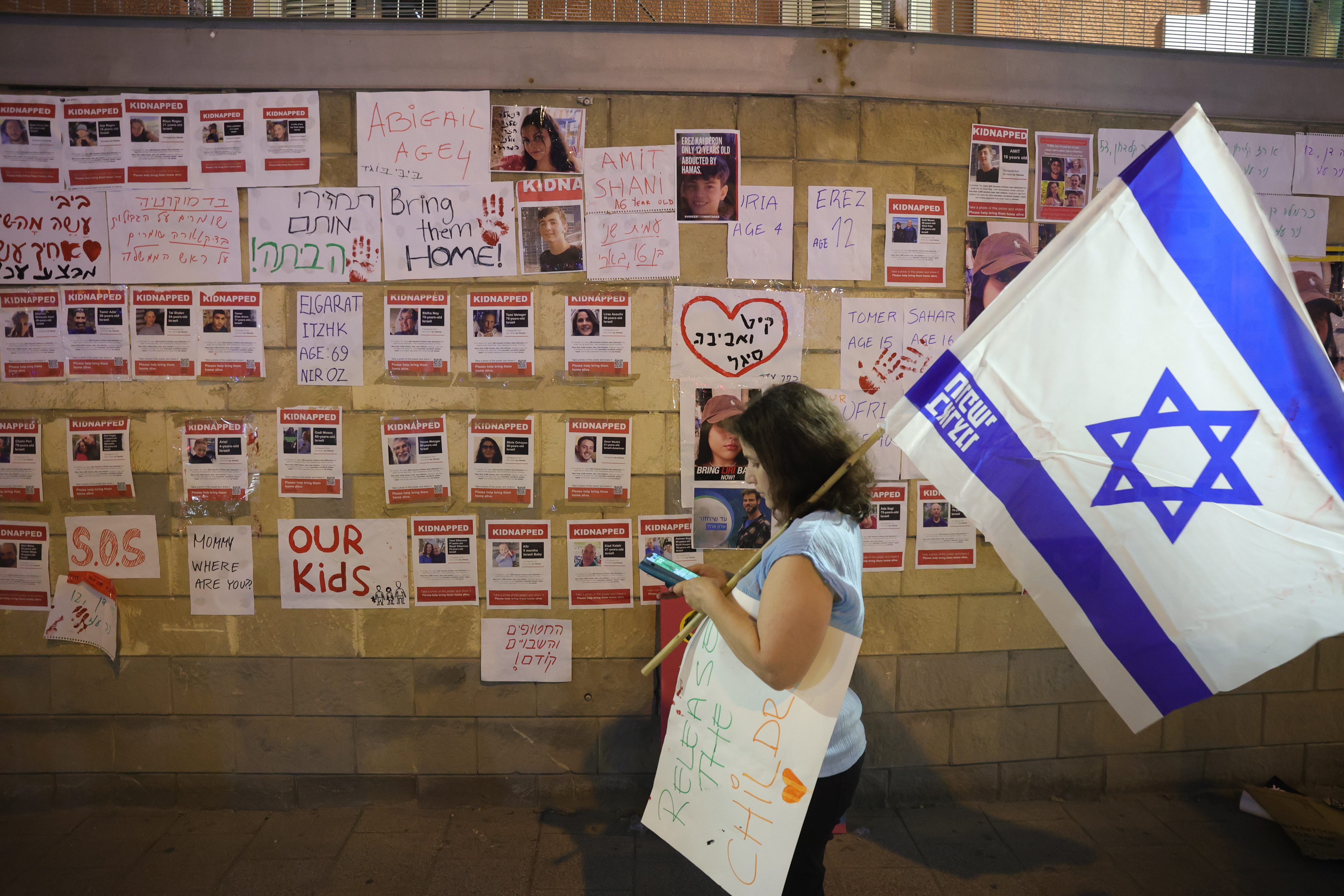Tel Aviv (Israel), 14/10/2023.- A person holding an Israeli flag walks past pictures of hostages hanging on a wall during a protest calling on the Israeli government to help rescue the hostages held by Hamas militants in Gaza, outside the Kirya military base in Tel Aviv, Israel, 14 October 2023. More than 1,300 Israelis have been killed and over 3,200 others injured, according to the IDF, after the Islamist movement Hamas launched an attack against Israel from the Gaza Strip on 07 October. More than 2,000 Palestinians have been killed and over 8,700 others injured in Gaza since Israel launched retaliatory air strikes, the Palestinian health ministry said. (Protestas) EFE/EPA/ABIR SULTAN