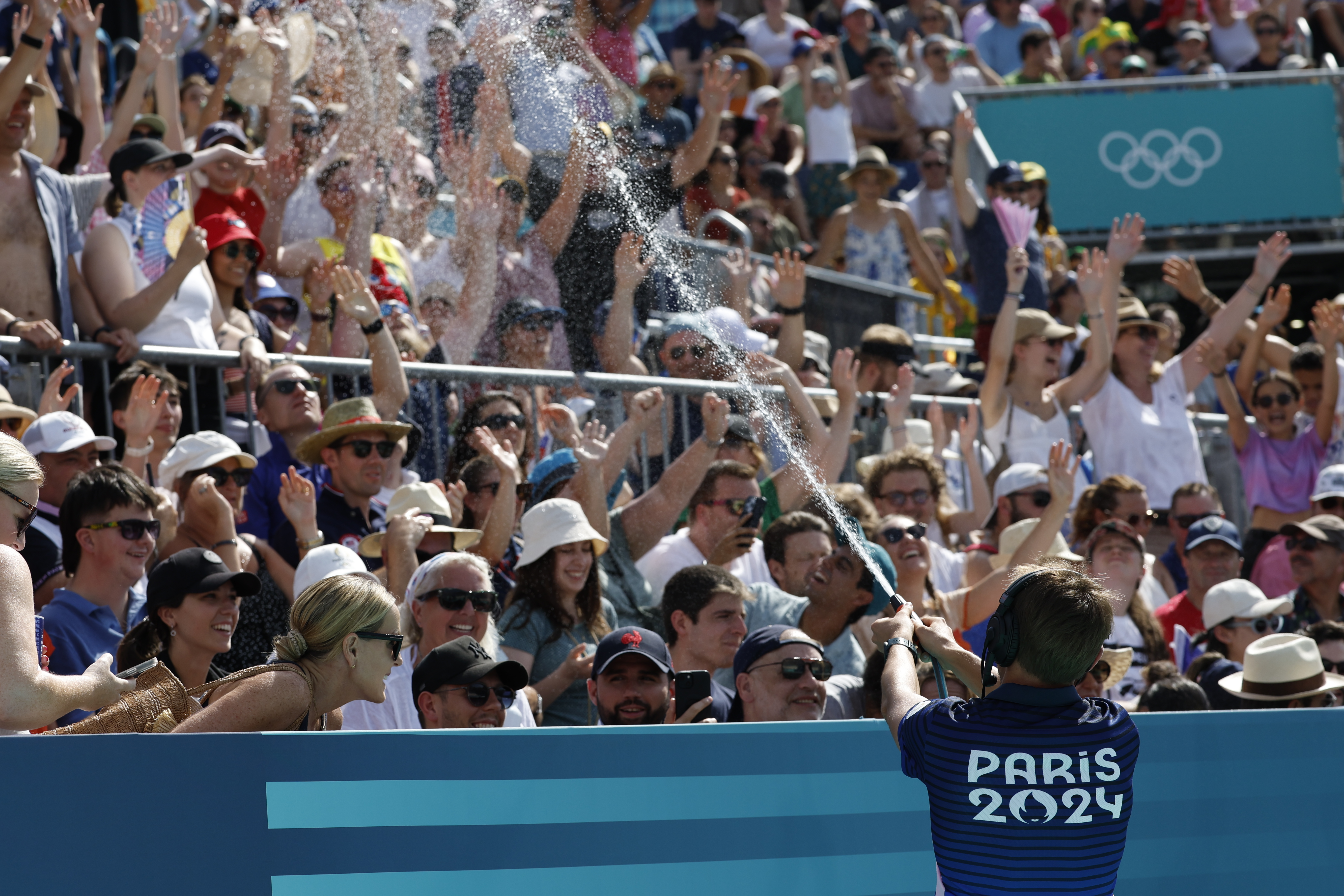 PARÍS, 30/07/2024.- Un miembro de la organización combate el calor rociando con agua a los asistentes al partido de voley playa femenino que disputan Italia y Egipto en el marco de los Juegos Olímpicos de París 2024, este martes en París. EFE/ Chema Moya