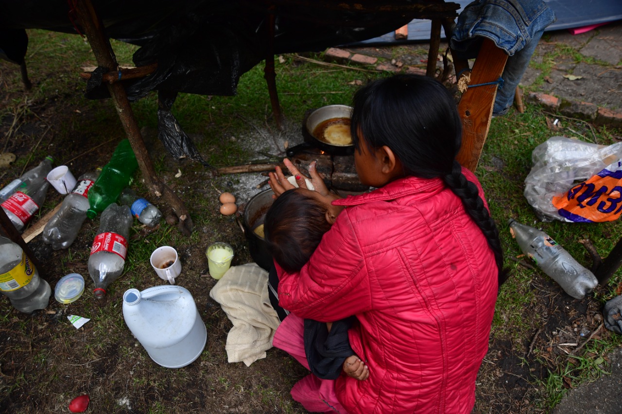 Mujer amasa arepas mientras sostiene a un pequeño. Hubo reportes de que cerca de 60 menores de edad enfrentaban problemas de salud.