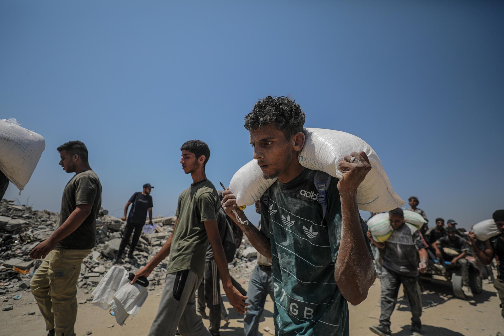 ZIKIM (-), 27/07/2025.- Internally displaced Palestinians carry bags of flour near a food distribution point in Zikim, northern Gaza Strip, 27 July 2025. The Israeli army declared a 'tactical pause' in military operations in parts of the Gaza Strip on 27 July, to facilitate the safe passage of humanitarian aid convoys. More than 130 Palestinians, the majority of whom children, have died of malnutrition in the Gaza Strip, the Palestinian Ministry of Health said on 27 July. EFE/EPA/MOHAMMED SABER
