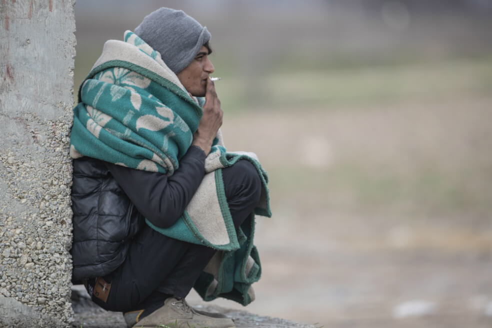 Un migrante paquistaní cubierto con una manta fuma un cigarrillo mientras descansa cerca de la frontera turco-griega, en Edirne, Turquía. / EFE