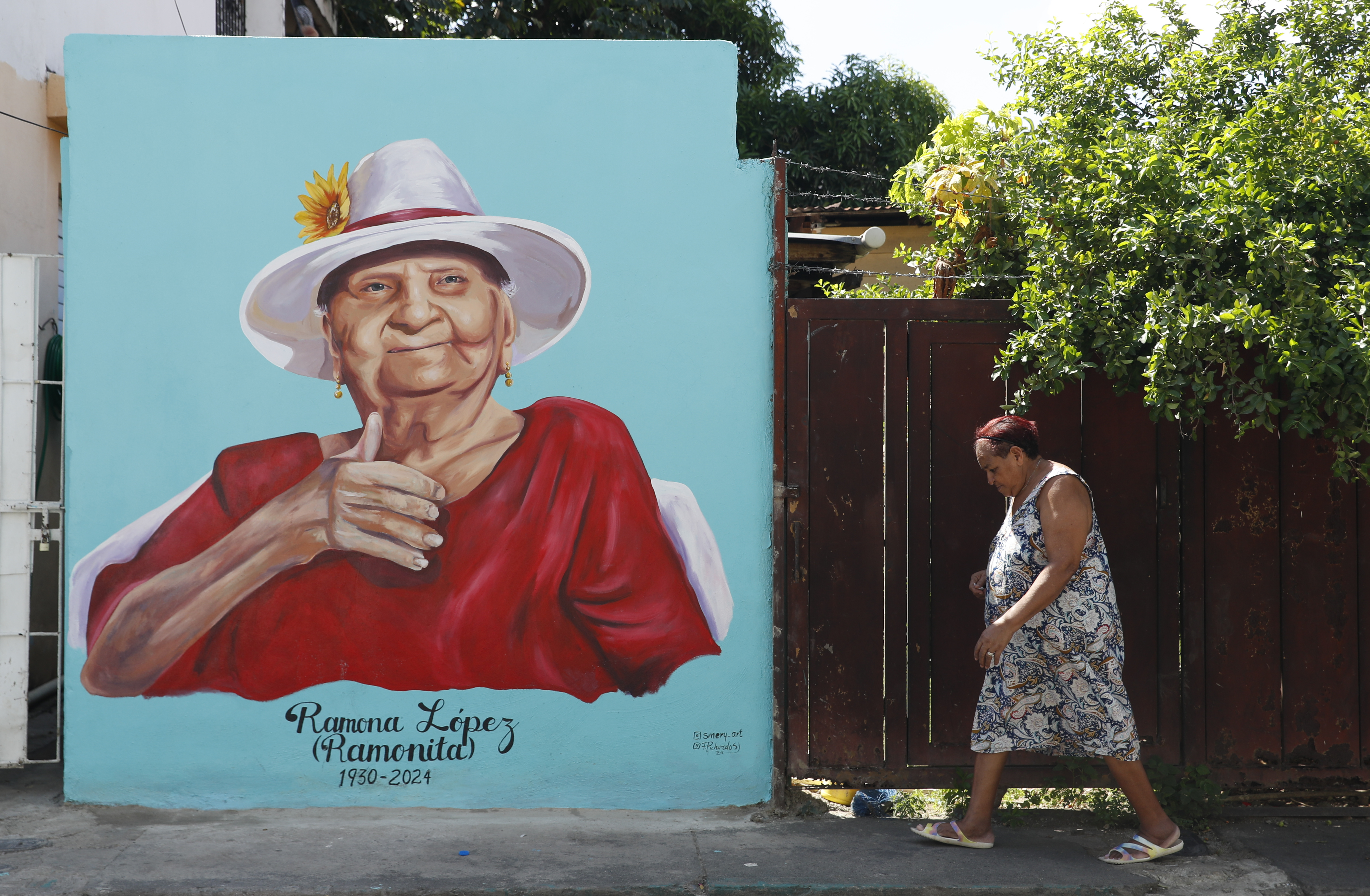 FOTOGALERÍA AMDEP9007. SANTIAGO DE LOS CABALLEROS (REPÚBLICA DOMINICANA), 18/10/2024.- Una mujer pasa frente a un mural en honor a Ramona López este viernes, en el barrio Los Pepines de Santiago de los Caballeros (República Dominicana). La historia, la cultura y el tradicional son aún palpitan en Santiago de los Caballeros. La ciudad, conocida sencillamente como Santiago por los dominicanos, mantiene el legado musical con el movimiento cultural el 'Son de Antonio Keka', al que se suma otro ritmo por estos días con la realización de la Copa Mundial sub-17 Femenina, que acoge hasta el próximo tres de noviembre. EFE/ Diana Sánchez