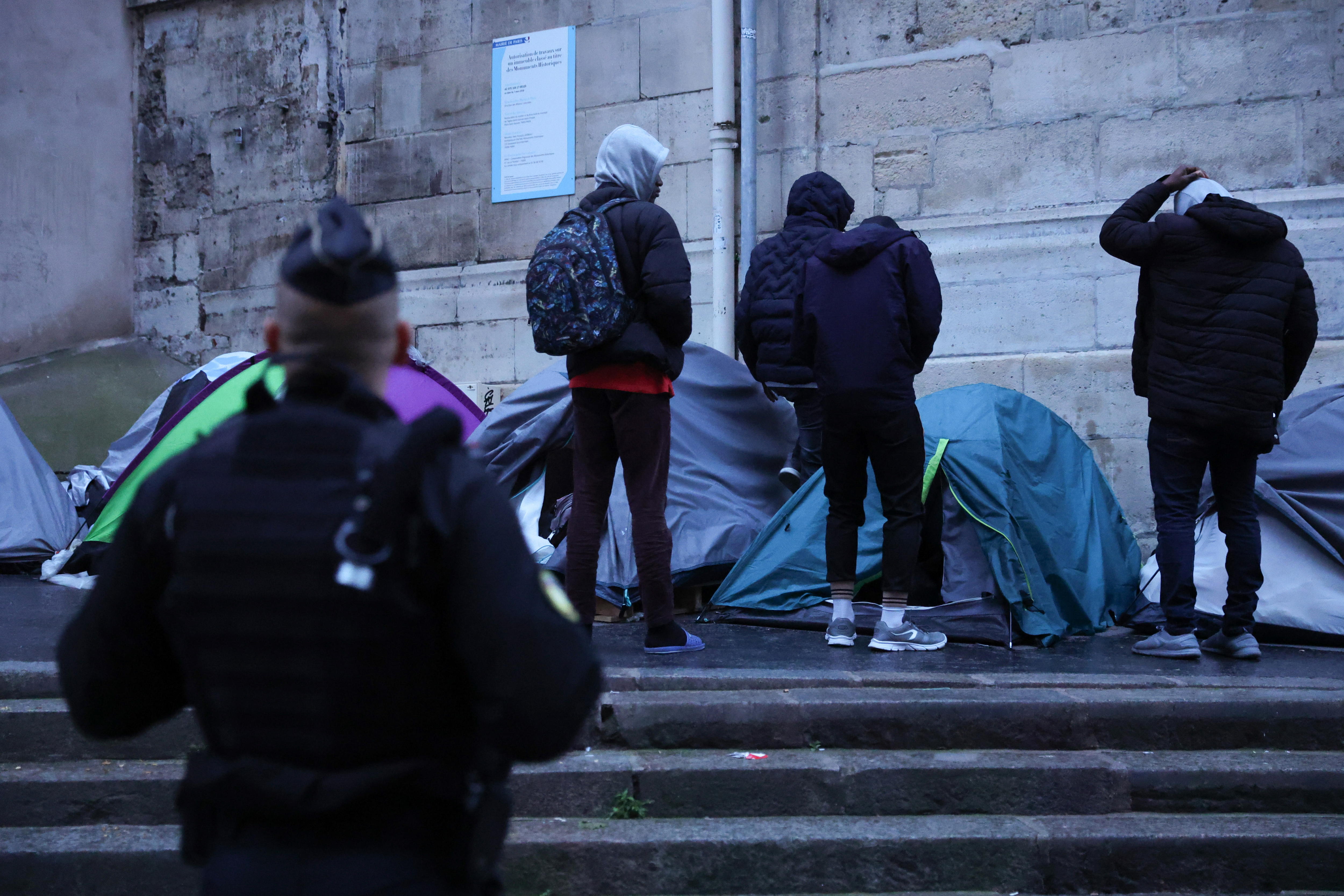 Paris (France), 30/04/2024.- A gendarme keeps watch as young migrants collect their belongings during their expulsion from a camp, where dozens of migrants live, near the town hall in Paris, France, 30 April 2024. The 80-tent camp is located between the Church of Saint Gervais and the Hotel de Ville de Paris. According to the prefecture's decree, the eviction is being carried out due to the lack of sufficient sanitary conditions and the increase of the security alert system 'Vigipirate' to the highest level. Humanitarian associations have denounced the evacuation as 'social cleansing' and a 'manhunt' in view of the Paris 2024 Olympic Games. (Francia) EFE/EPA/Teresa Suarez