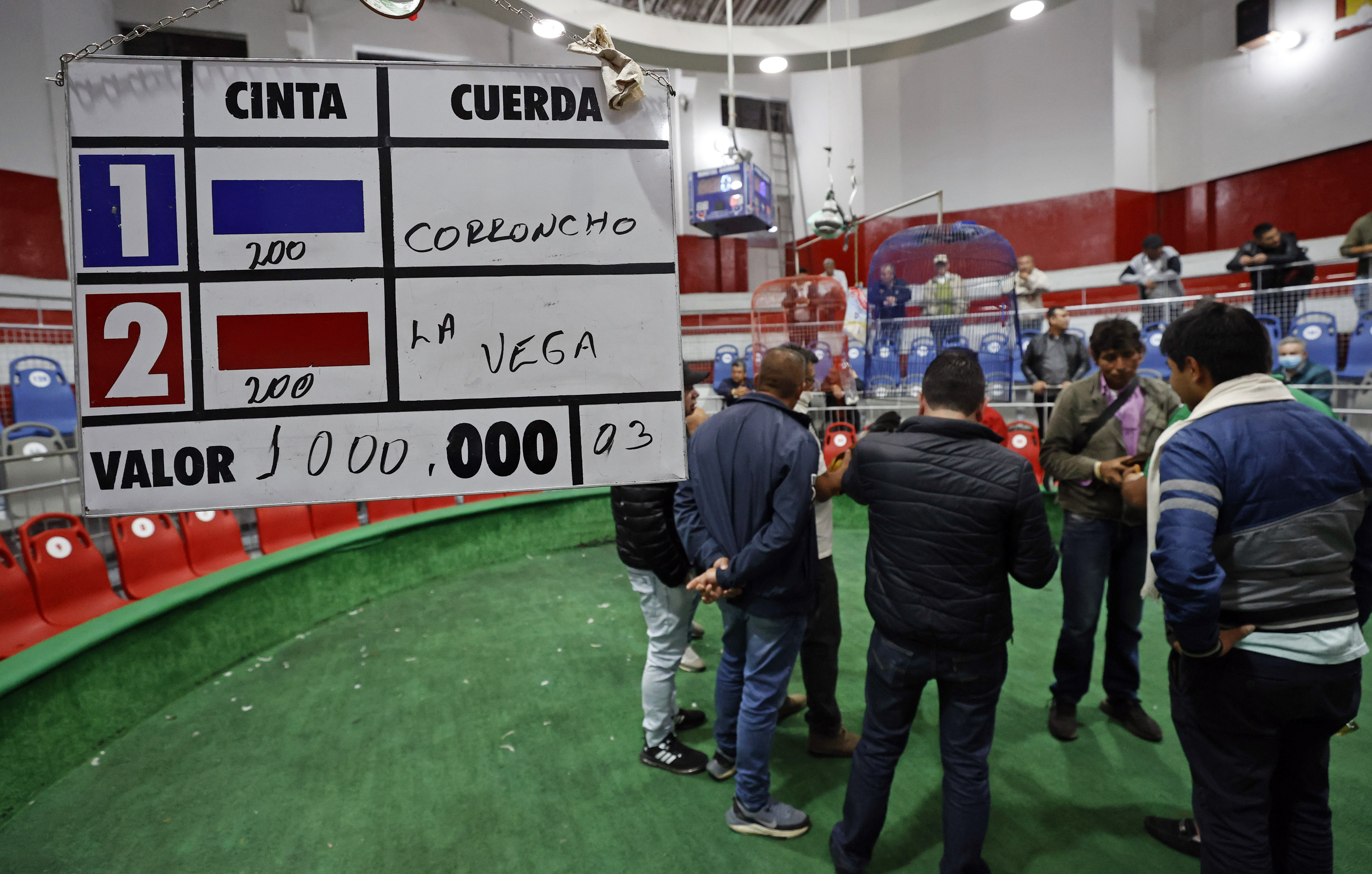 ACOMPAÑA CRÓNICA: COLOMBIA ANIMALES. BOG300. BOGOTÁ (COLOMBIA), 02/11/2022.- Varios hombres esperan previo a una pelea de gallos, el 21 de octubre de 2022, en Bogotá (Colombia). En la pizarra de la entrada, con una caligrafía casi perfecta, los dueños de la gallera van anotando los rivales de la noche: los gallos no tienen nombre, no es relevante, pero sí lo es el peso y el tamaño para enfrentarlos en "condiciones justas" en un espectáculo que ha quedado atrapado en el tiempo en Colombia.EFE/ Mauricio Dueñas Castañeda