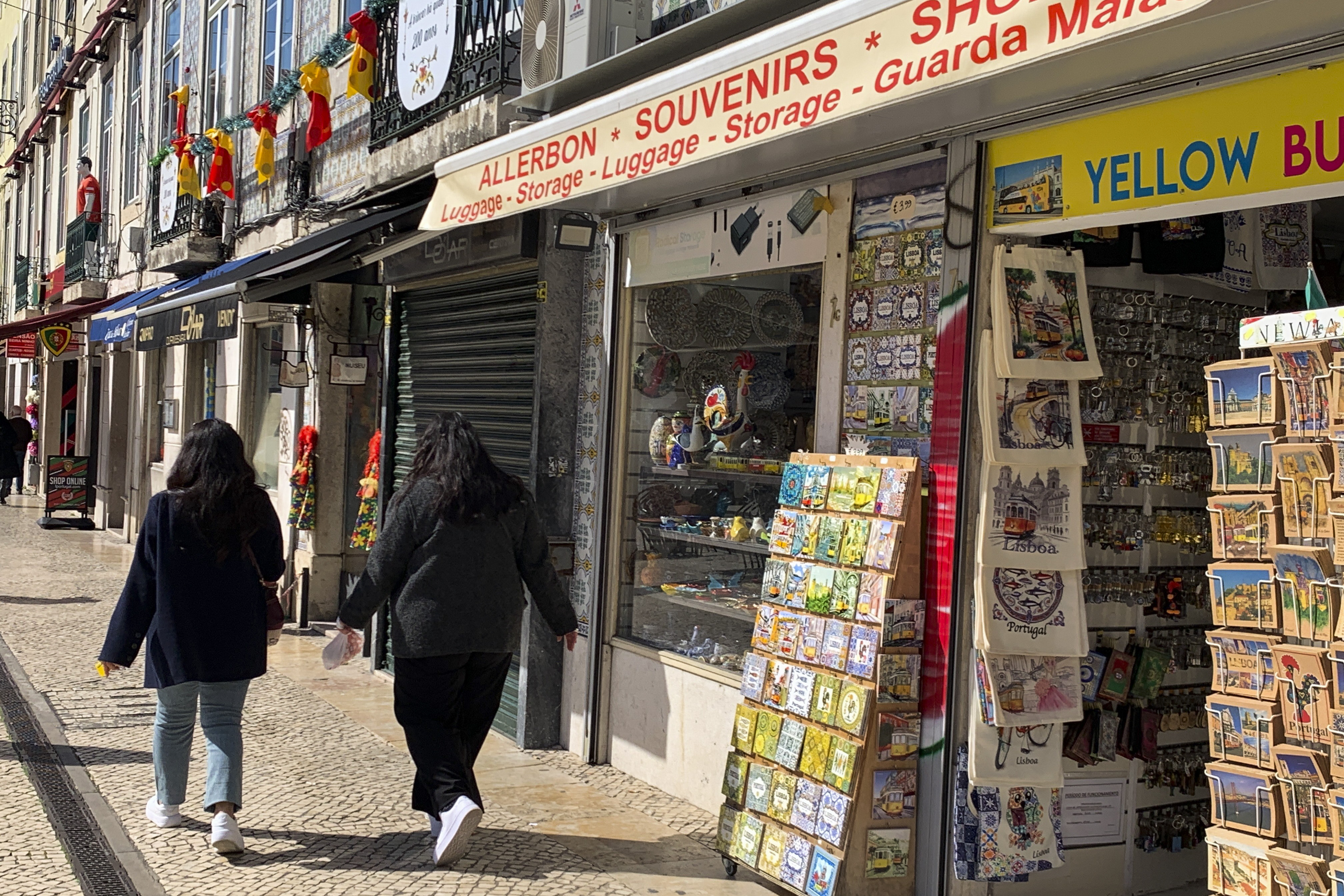 LISBOA, 26/02/2025. Dos jóvenes pasean junto a una de las decenas de tiendas de 'souvenirs' del centro de Lisboa. El Ayuntamiento de Lisboa aprobó este miércoles una moción para pedir al Gobierno portugués que realice cambios legales para limitar el número de tiendas de 'souvenirs' en su casco histórico. EFE/Carlos Caselles