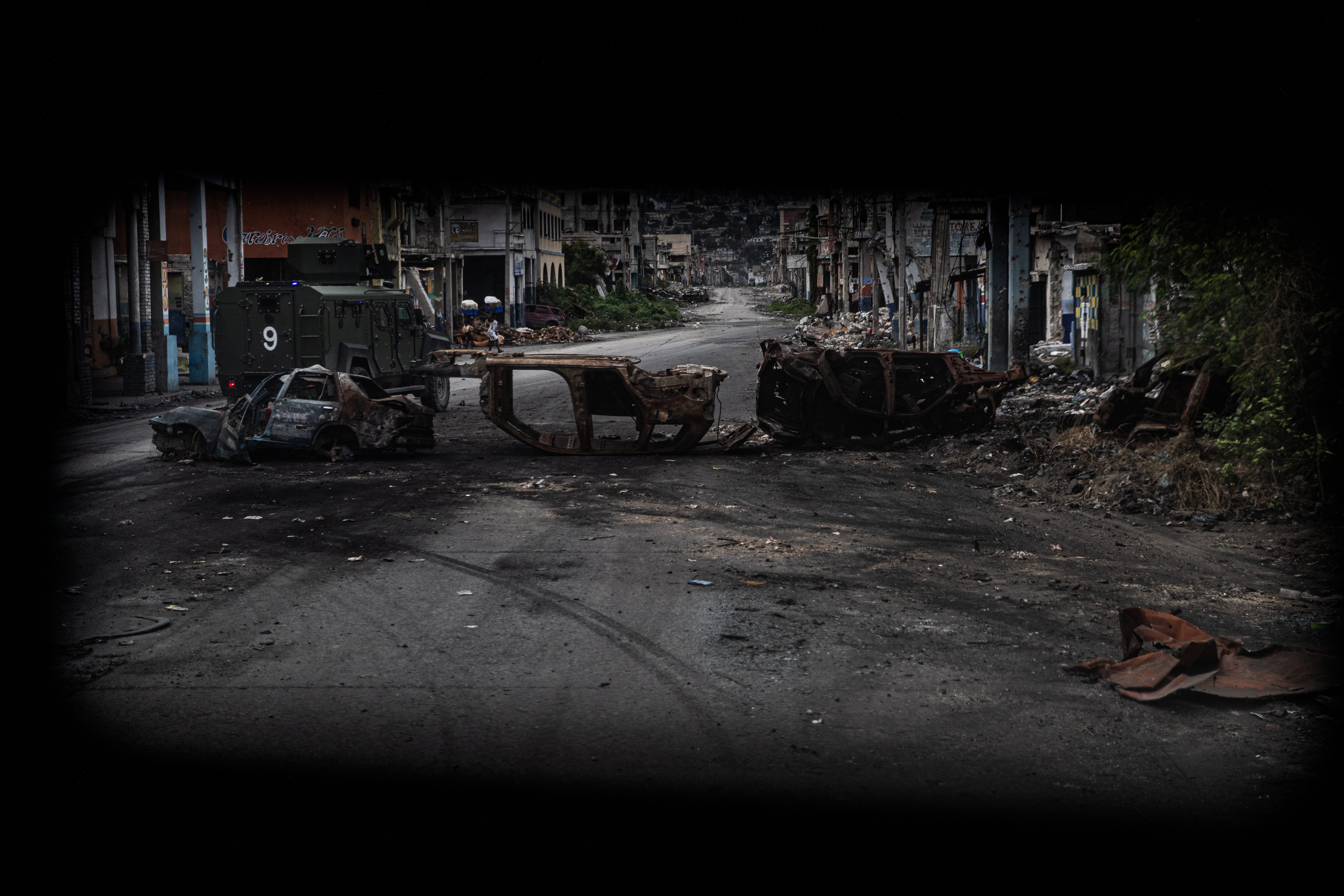 Un vehículo policial rodea automóviles incendiados por bandas armadas y utilizados como barricada durante los enfrentamientos de la semana pasada con las fuerzas de seguridad haitianas en una calle desierta del centro de la ciudad, visto desde un vehículo policial blindado durante una patrulla, en Puerto Príncipe el 16 de enero de 2026.