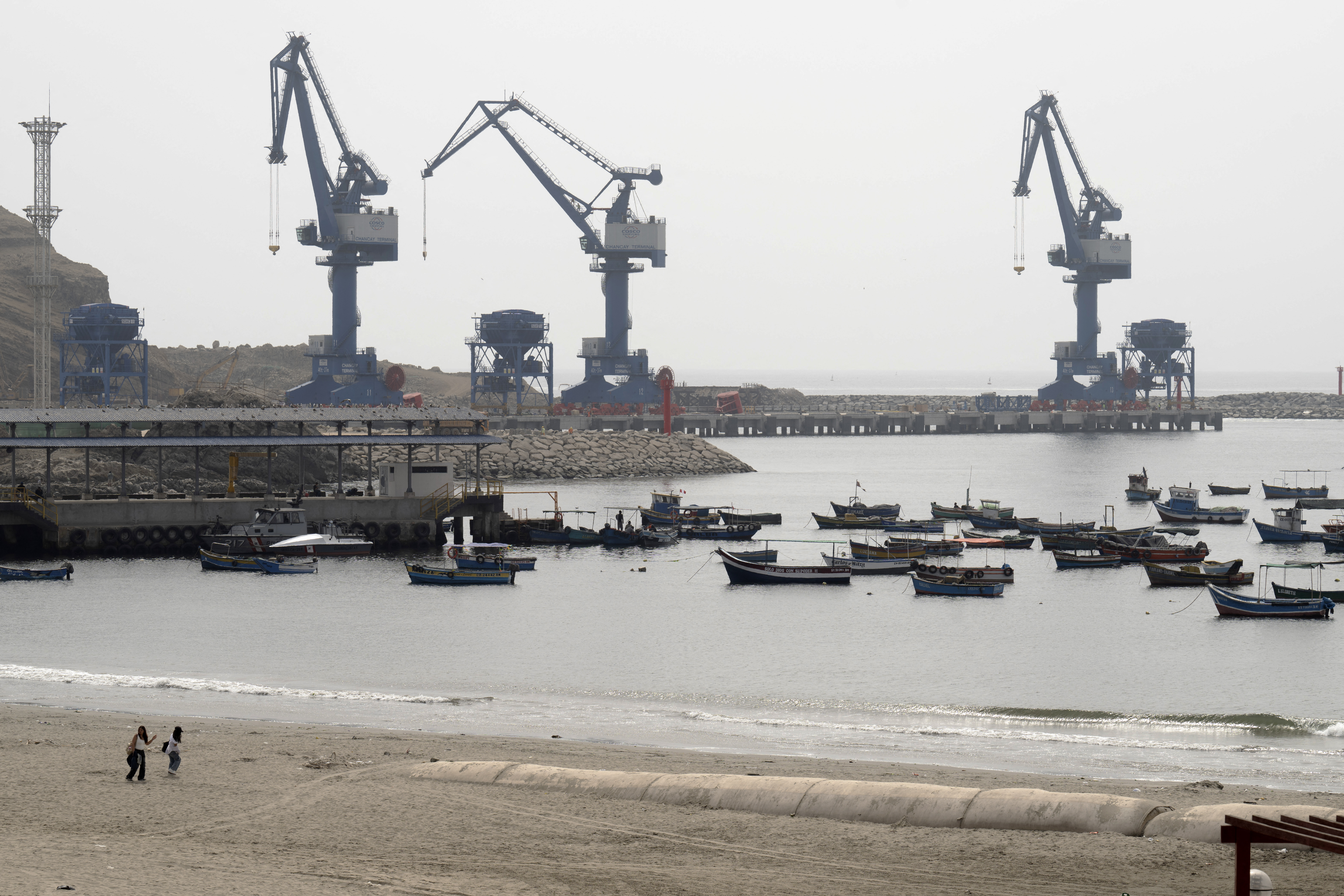 The Chancay "megaport" cranes are seen from the town's harbor, where traditional fishing boats rest, 78 kilometers north of the Peruvian capital Lima, on October 29, 2024.