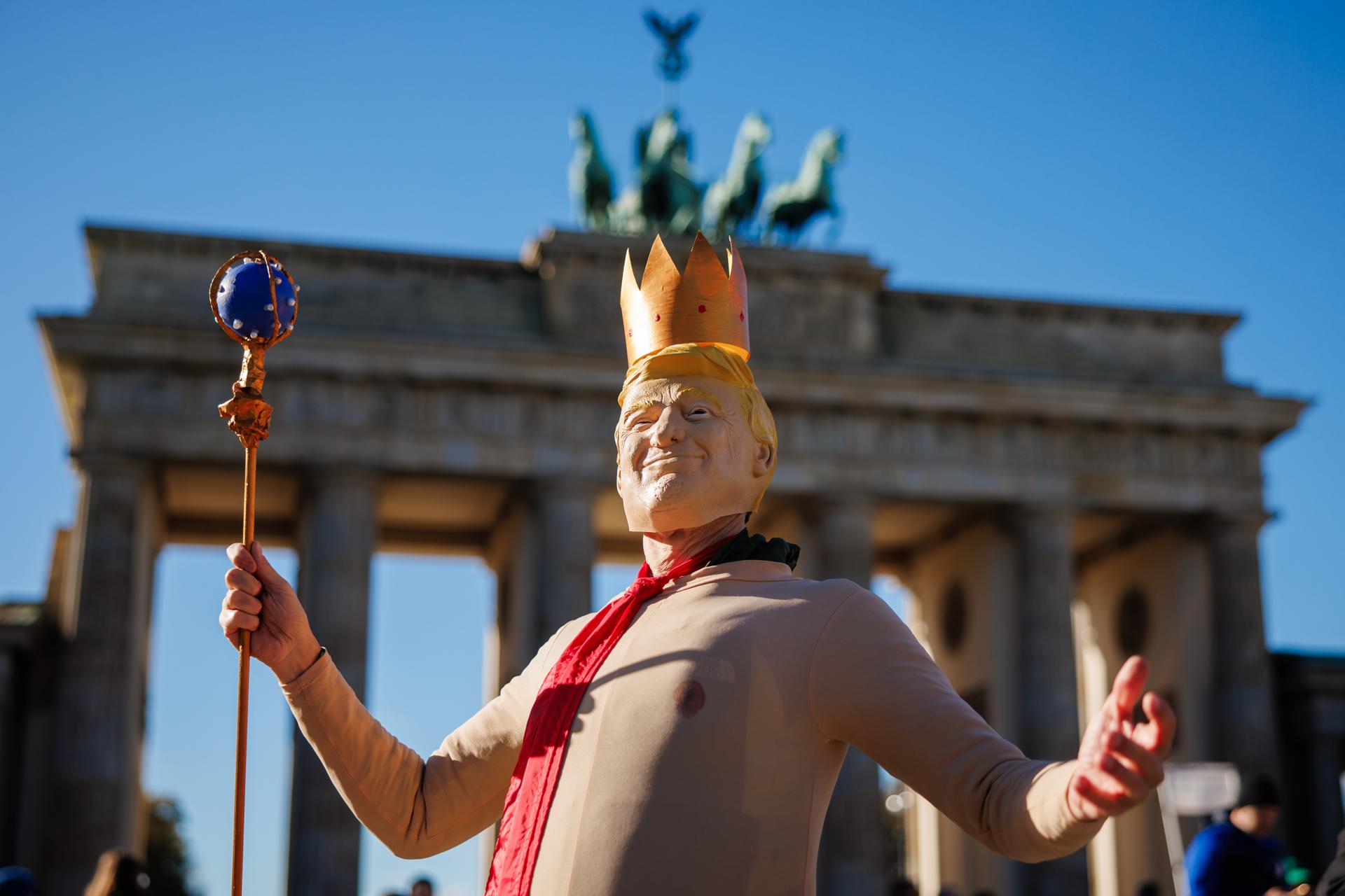 Una persona viste un disfraz del presidente estadounidense Donald J. Trump con una corona en la cabeza durante una manifestación frente a la Puerta de Brandeburgo en Berlín.
