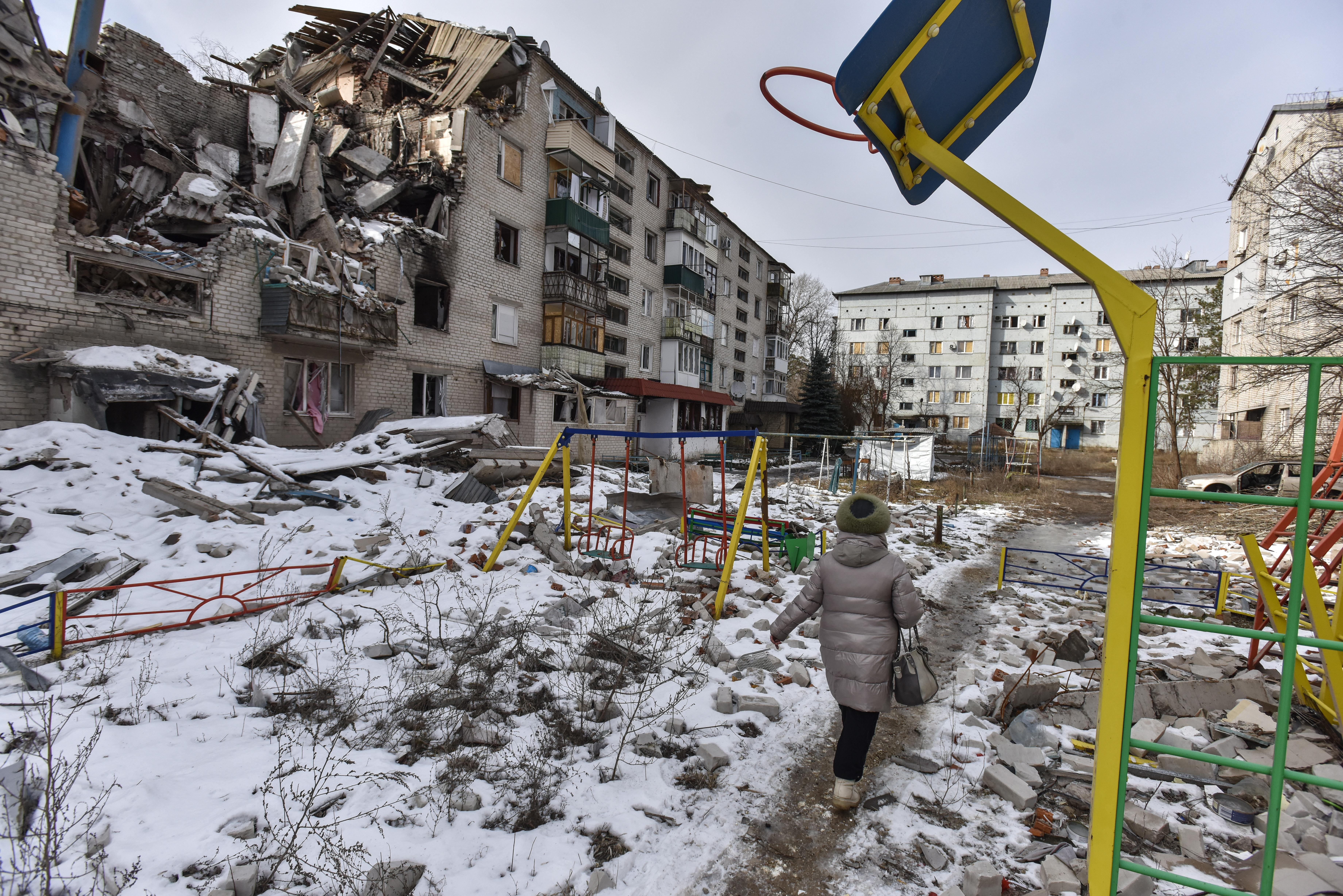 -FOTODELDÍA- EA5110. SVIATOHIRSK, 24/02/2023.- Una mujer pasa por un parque infantil frente a un edificio en ruinas por un ataque ruso, en Sviatohirsk, en la región de Donetsk, Ucrania. Este viernes se cumple el primer año de la guerra en Ucrania. EFE/ Oleg Petrasyuk