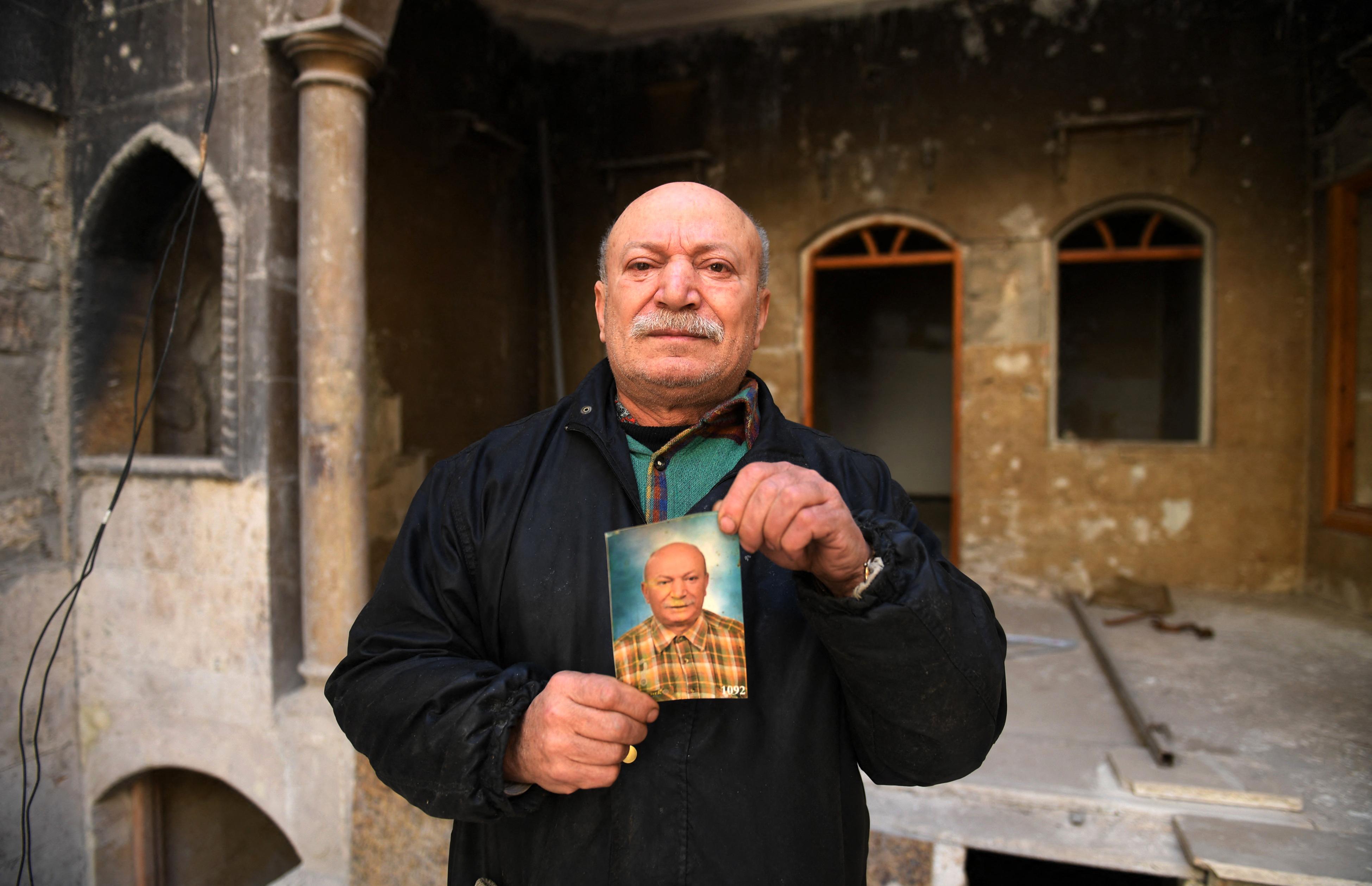 Ahmed Nashawi, también conocido como Abu Abdo, posa con un retrato de sí mismo de hace diez años atrás frente a su casa destruida en la ciudad de Alepo, en el norte de Siria, el 22 de febrero de 2021. El hombre de unos cincuenta años, una vez uno de los pescaderos más populares de la ciudad, dijo que su casa y su tienda en la plaza Sahat al-Hatab fueron destruidas en enfrentamientos entre rebeldes y combatientes progubernamentales en 2015.