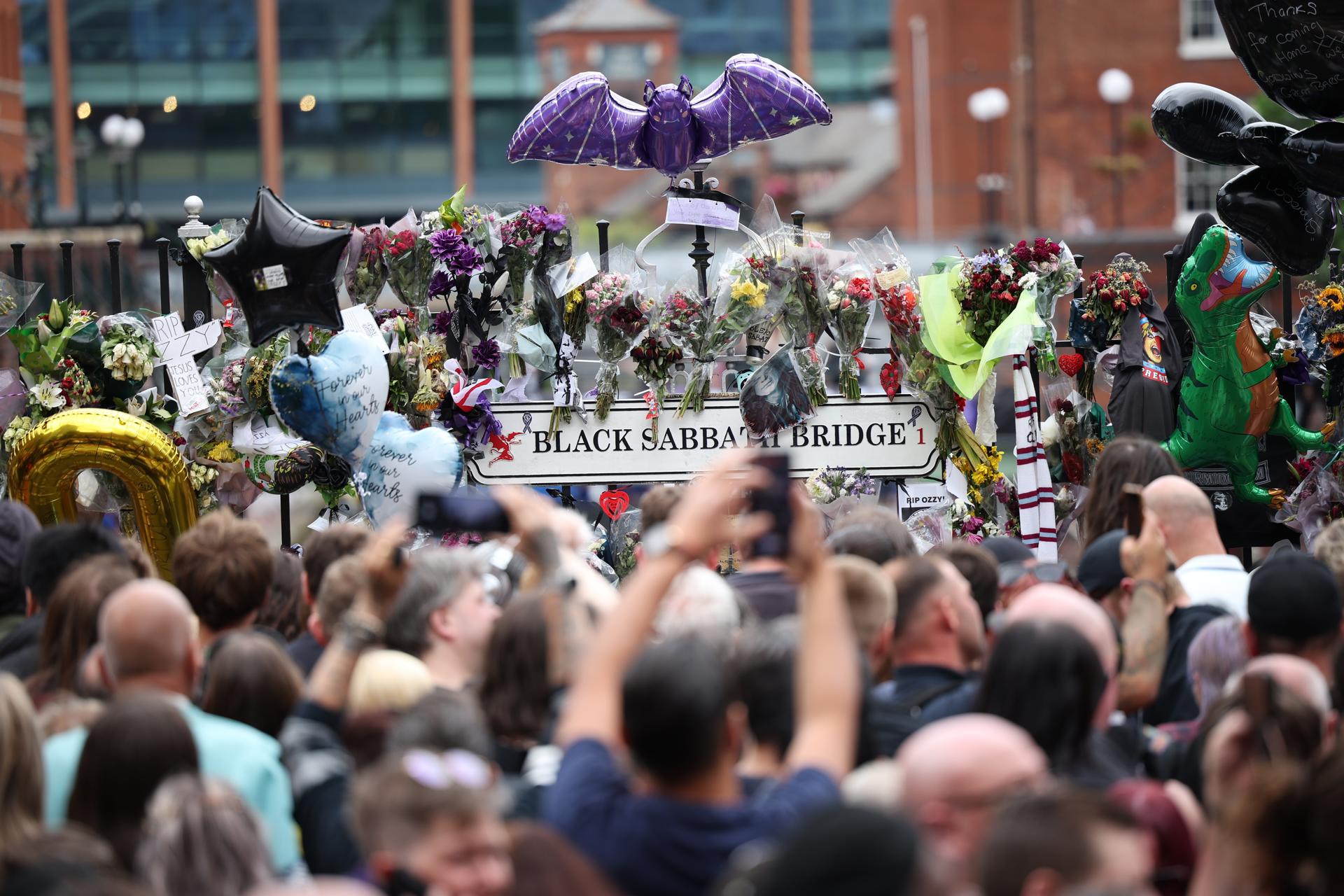 BIRMINGHAM (United Kingdom), 30/07/2025.- Fans take pictures of tributes to Ozzy Osbourne at the Black Sabbath bench and Bridge after watching Osbourne's funeral cortege in Birmingham, Britain, 30 July 2025. Osbourne died aged 76 on 22 July 2025, weeks after performing his final concert with Black Sabbath. He had been diagnosed with Parkinson's disease in 2019. (Reino Unido) EFE/EPA/ADAM VAUGHAN