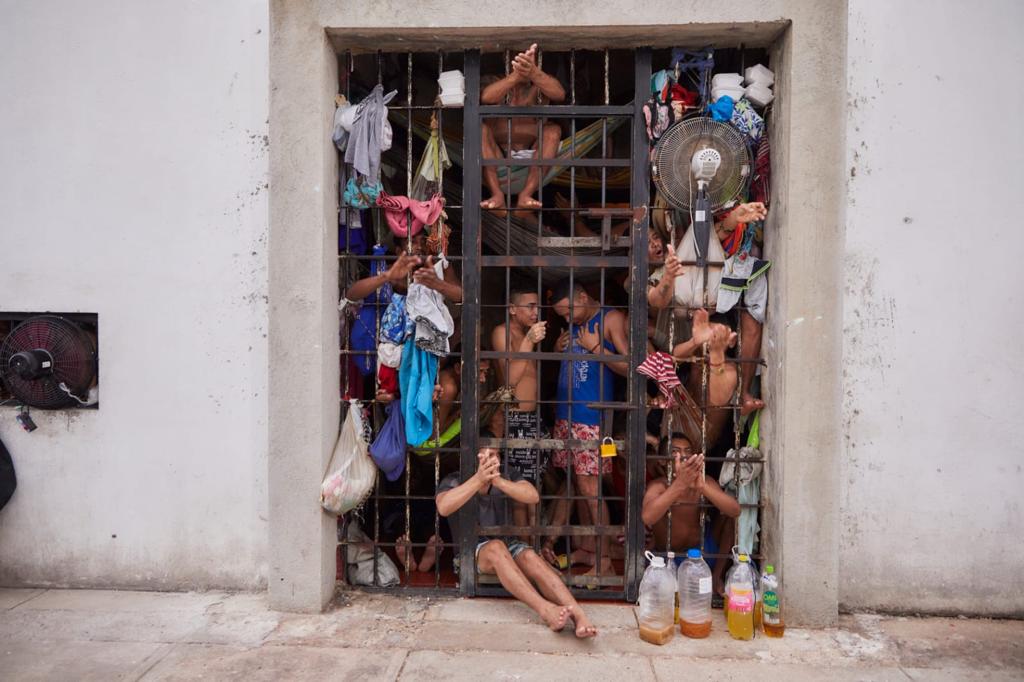 Varios hombres tras una reja. Se ven un ventilado y varias botellas de plástico con líquido, en el suelo.