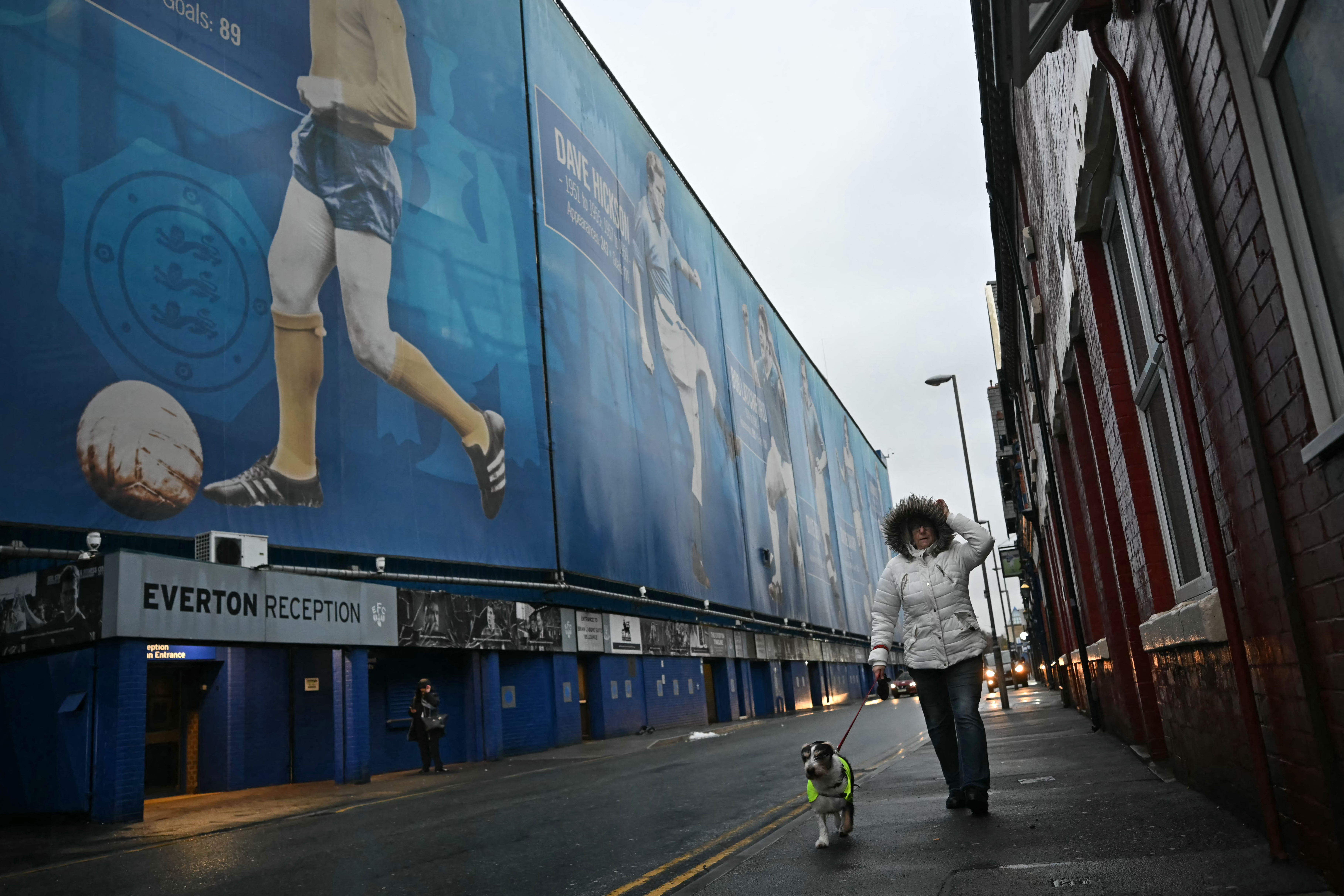A dog-walker passes the ground as news of the postponement of the English Premier League football match between Everton and Liverpool spreads, outside Goodison Park in Liverpool, north west England on December 7, 2024.