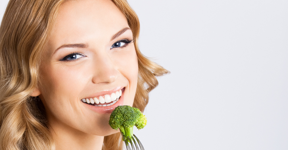 Portrait of happy smiling young beautiful woman with healthy vegetarian salad, over gray background