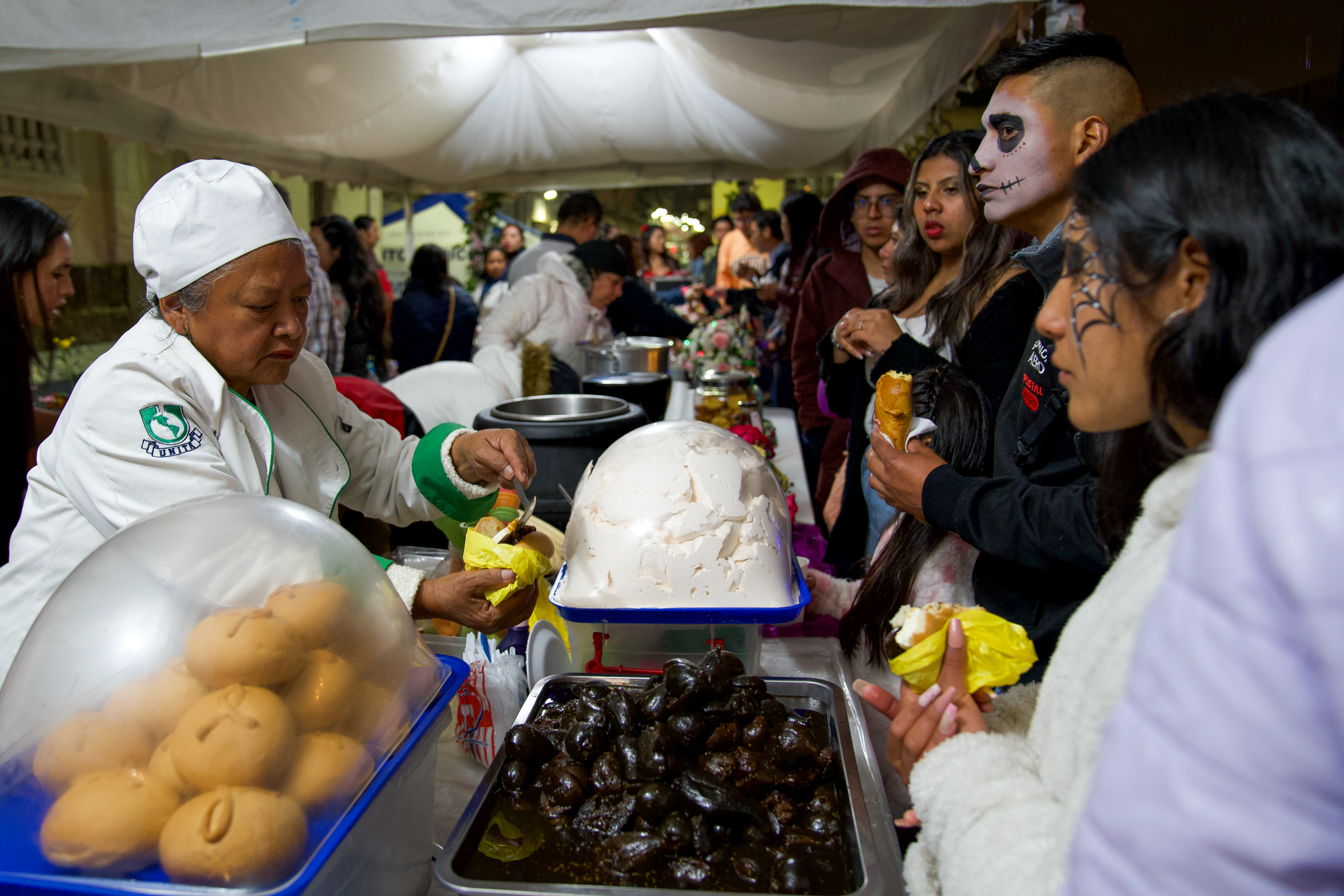 QUI01. QUITO (ECUADOR) 01/11/2024.- Personas disfrazadas consumen alimentos el pasado jueves en Quito (Ecuador). Las tradicionales 'guaguas' de pan, acompañadas de su inseparable colada morada, y personajes de las leyendas negras de Quito se dan cita este fin de semana en una nueva edición del festival 'Más allá de la vida', donde la capital ecuatoriana ensalza sus tradiciones en torno al Día de Difuntos. EFE/Vicente Costales