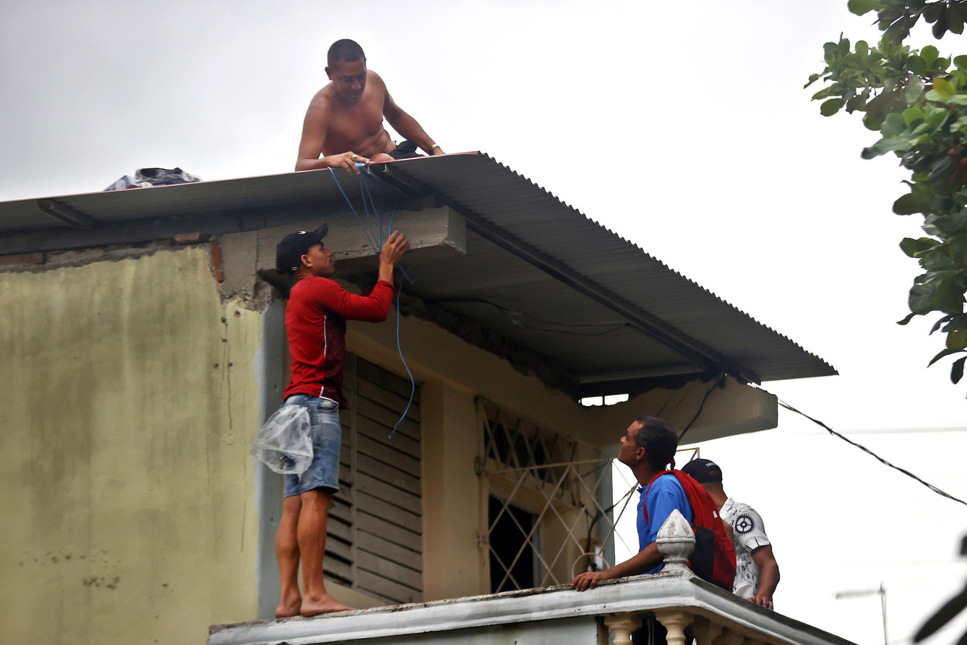 AME2711. SANTIAGO DE CUBA (CUBA), 28/10/2025.- Personas trabajan para asegurar el techo de una vivienda ante la posible llegada del huracán Melissa este martes, en Santiago de Cuba (Cuba). Tras su paso por la isla, se prevé que Melissa cruce el sureste de Cuba el miércoles y llegue a las Bahamas el jueves. EFE/ Ernesto Mastrascusa