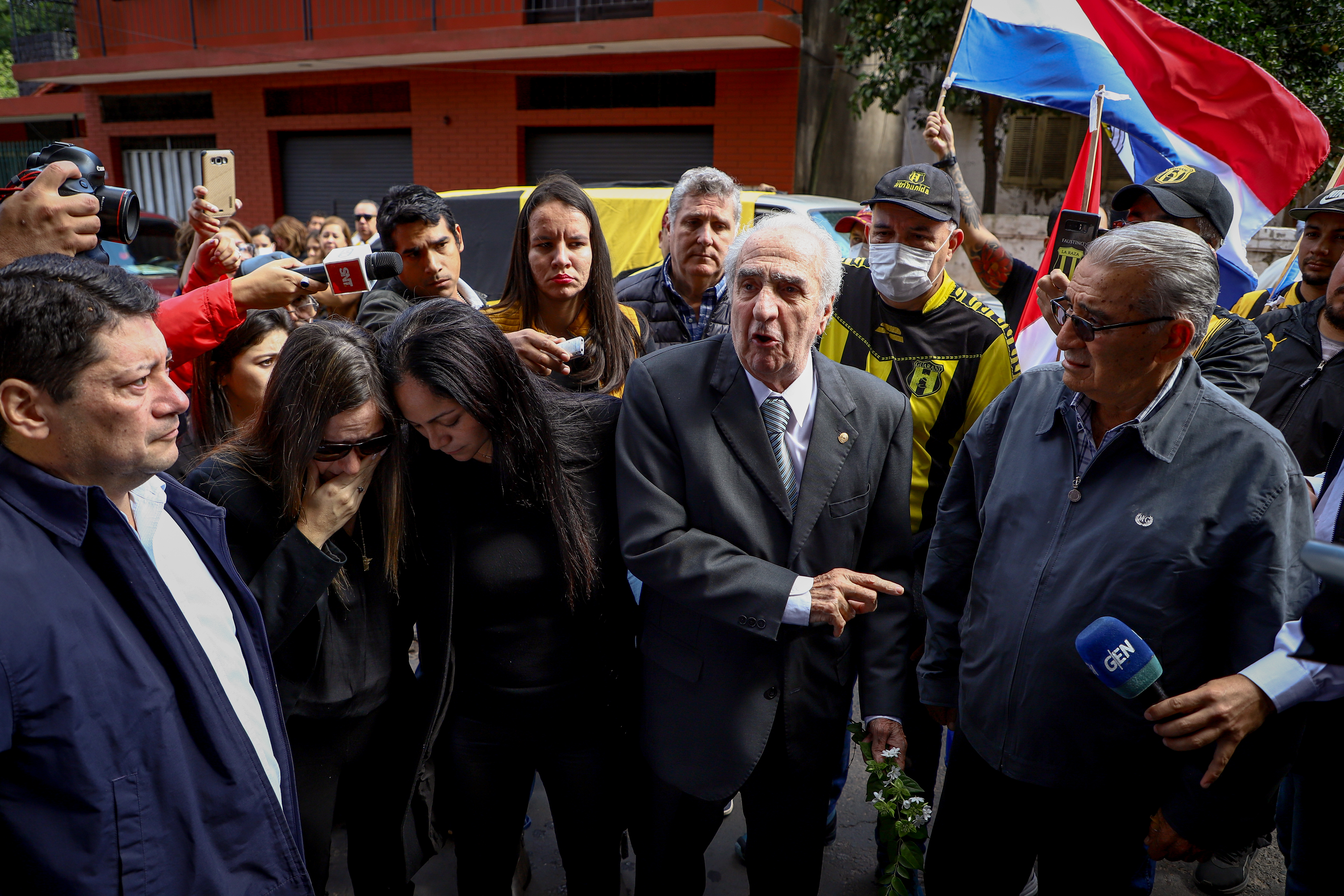 AME9535. ASUNCIÓN (PARAGUAY), 15/05/2022.- Claudia Pecci (2-i), Mónica Pecci (3-i) y Francisco Pecci (c), esposa, hermana y padre del asesinado fiscal Marcelo Pecci, se lamentan hoy frente a la sede del Club Guaraní en Asunción (Paraguay). Marcelo Pecci, el fiscal asesinado en Colombia y a quien este domingo despiden los paraguayos, se erigió públicamente en implacable contra el delito, pero para sus allegados era el hombre de buen humor, apasionado por el fútbol y la aviación. Asimismo, dirigentes, futbolistas y fanáticos del Club Guarani le rinden un homenaje al fiscal Pecci en la sede del club. EFE/ Nathalia Aguilar
