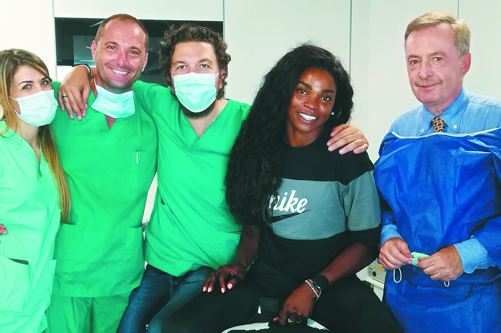 Personal médico con uniforme verde y con ellos está Caterine Ibargüen con camiseta negra, cabello largo y amplia sonrisa. Están en un recinto cerrado.