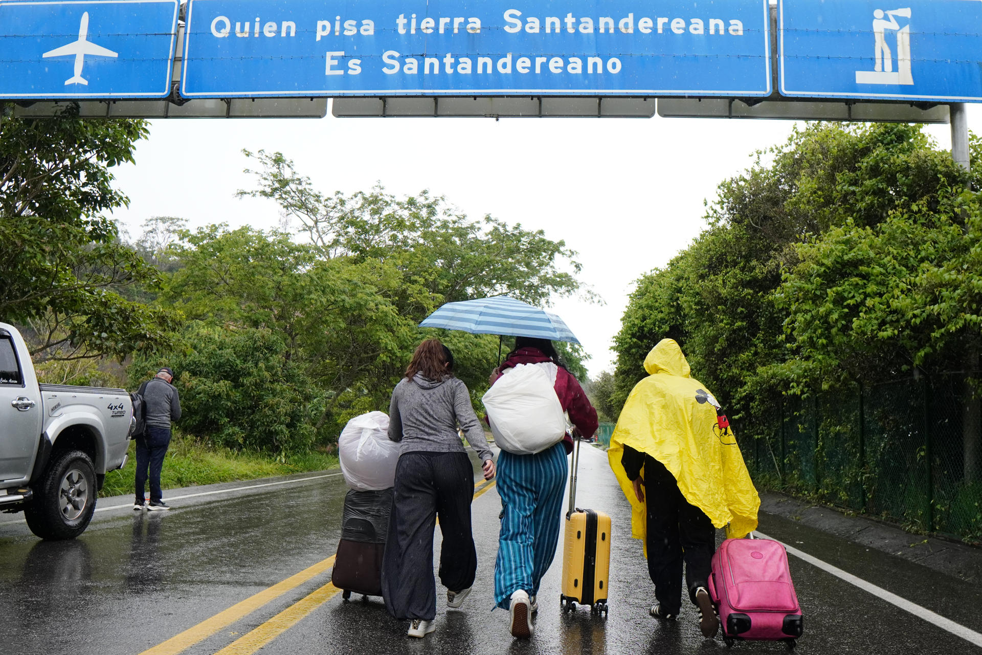 FOTODELDÍA AME3146. LEBRIJA (COLOMBIA), 13/04/2026.- Viajeros afectados por bloqueos caminan con sus maletas mientras la vía permanece cerrada por manifestantes que protestan contra el incremento de los avalúos catastrales, este lunes en la carretera que conduce al Aeropuerto Internacional Palonegro, en Lebrija (Colombia). EFE/ Marco Valencia
