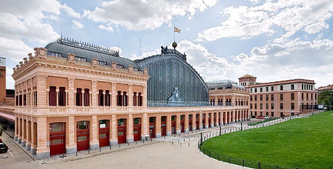 La Estación Madrid Puerta de Atocha Almudena Grandes es mucho más que un nodo ferroviario: es un espacio donde historia, arquitectura y naturaleza se encuentran. Inaugurada en 1851 como la antigua estación de Mediodía y transformada en 1992, hoy combina su imponente estructura de hierro del siglo XIX con un sorprendente jardín tropical interior que ocupa las antiguas vías. Convertida en el principal punto de conexión ferroviaria de España, Atocha no solo articula viajes por todo el país, sino que también ofrece a los viajeros una pausa verde en medio del movimiento constante.