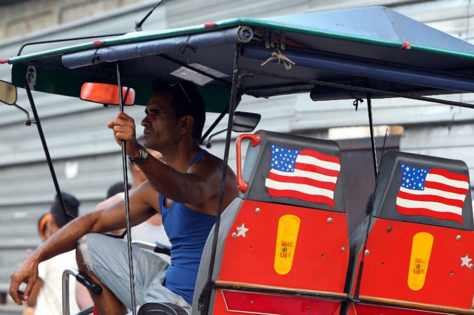 Un mototaxista cubano exhibe una bandera de Estados Unidos. / AFP