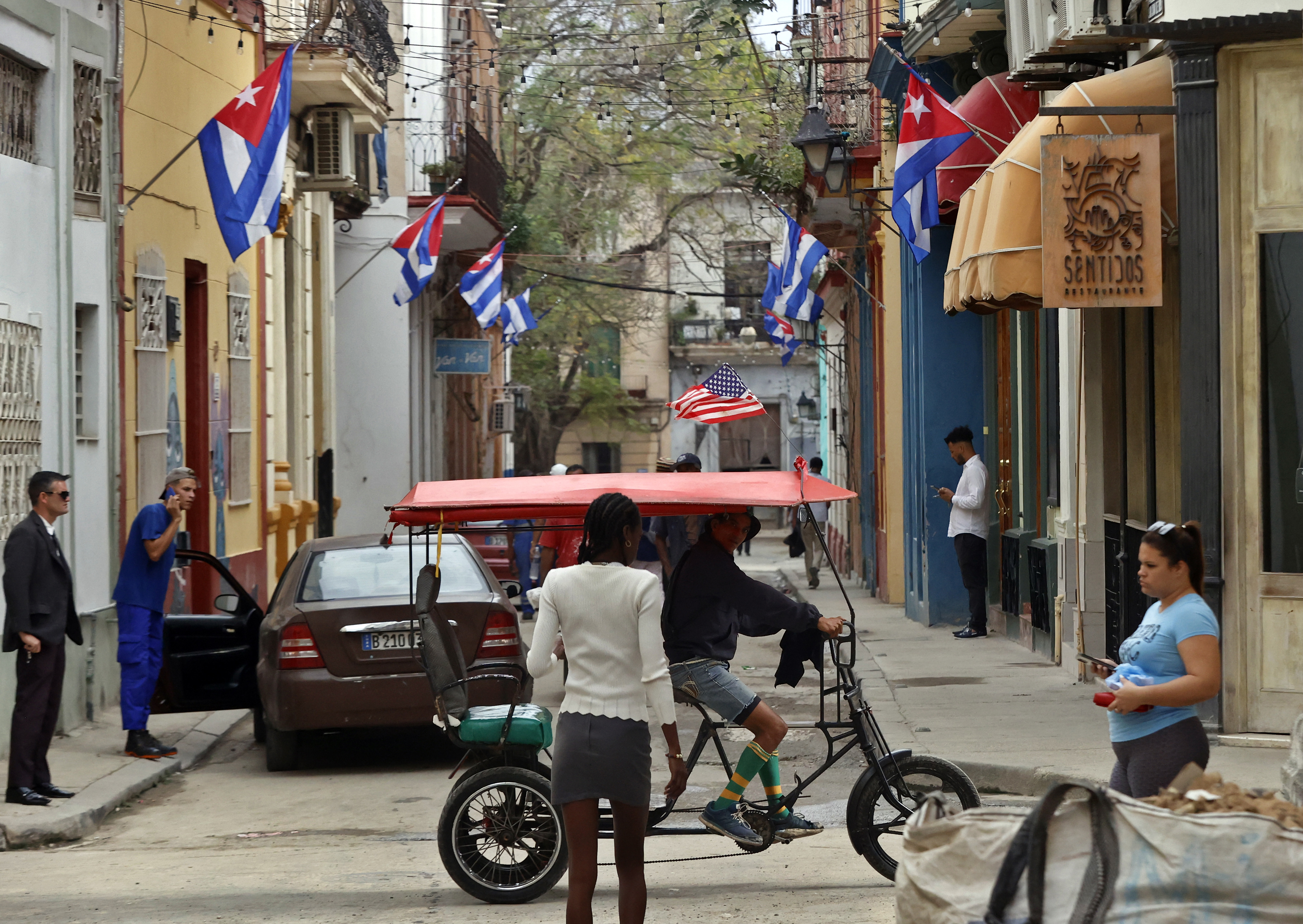 AME1517. LA HABANA (CUBA), 15/01/2025.- Personas transitan por una calle decorada con banderas de Cuba este miércoles, en La Habana (Cuba). Las autoridades cubanas aclararon este miércoles que las 553 personas que saldrán de las cárceles de la isla no han sido ni indultadas ni amnistiadas -sino, técnicamente, excarceladas- y que, por tanto, "pueden regresar a la prisión" si no cumplen una serie de "requisitos", como una "buena conducta". EFE/ Ernesto Mastrascusa