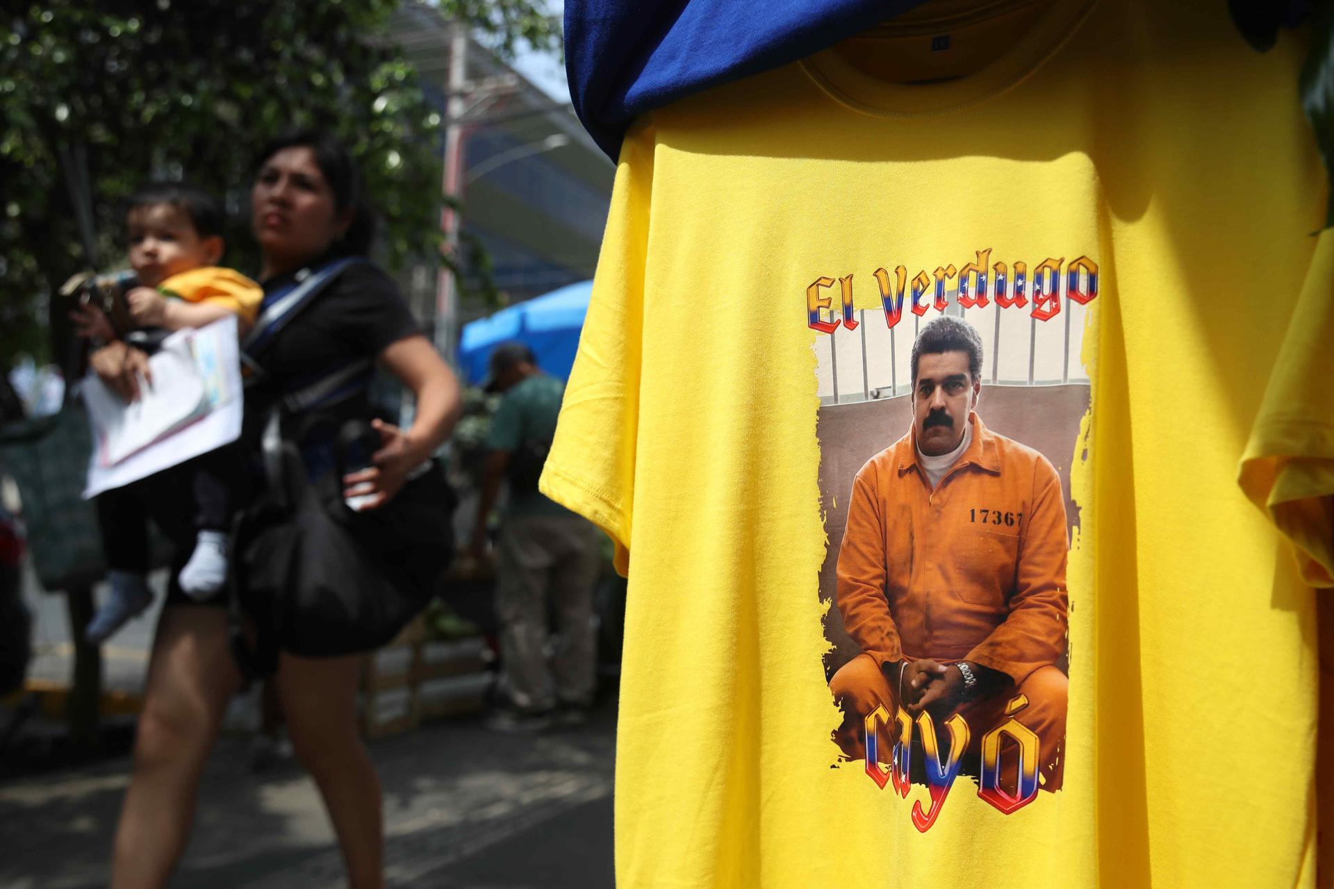 AME2707. LIMA (PERÚ), 06/01/2026.- Una mujer camina frente a una camiseta con una imagen de la captura del presidente de Venezuela, Nicolás Maduro, este martes, en Lima (Perú). Las imágenes de la captura de Maduro han pasado a estamparse en camisetas y prendas de vestir, diseños que se han puesto de moda entre la comunidad venezolana residente en Perú para celebrar este acontecimiento de su país. EFE/ Paolo Aguilar