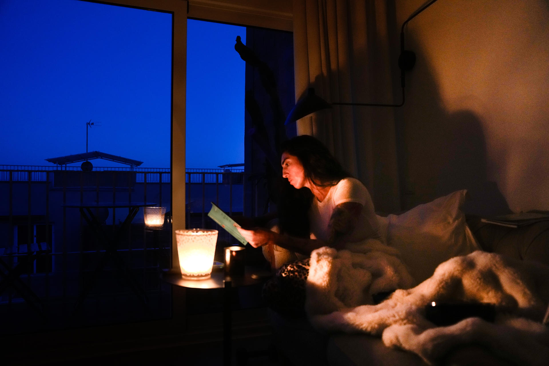 GRAFCAT7652. EL MASNOU (BARCELONA), 29/04/2025.- Una mujer lee en su casa con ayuda de una vela esta madrugada en la localidad de El Masnou (Barcelona) durante el corte de suministro eléctrico que ha afectado a España y que ha dejado sin servicio el metro y el tranvía de Barcelona y todas las líneas de ferrocarril, y sin red de teléfonos móviles ni internet. EFE/Enric Fontcuberta