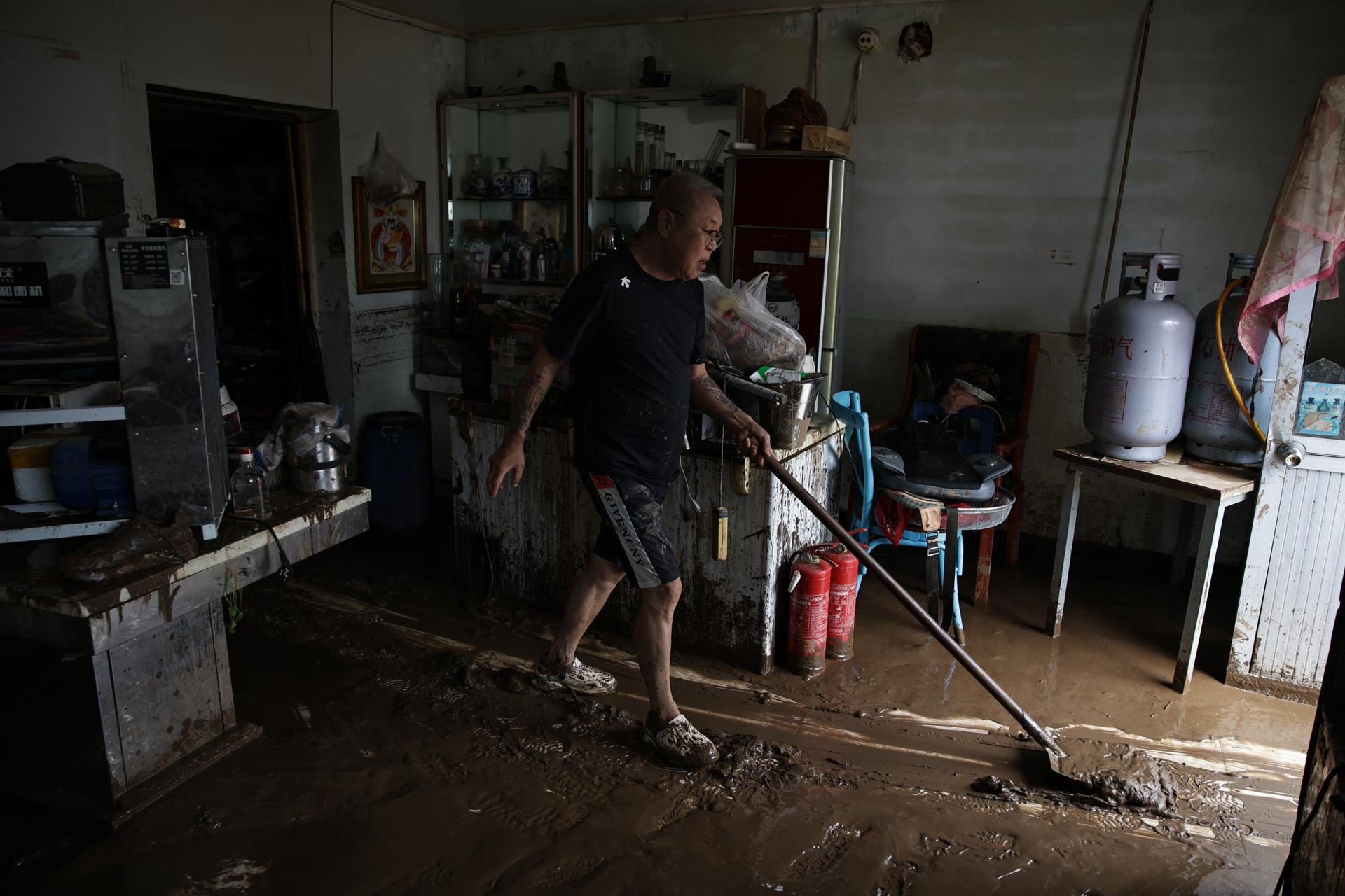 BEIJING (China), 29/07/2025.- A man removes mud at the entrance of a restaurant in a flooded street at Taishitun, in the district of Miyun, Beijing, China, 29 July 2025. The floods brought on by the rains in past days in Beijing resulted in the deaths of thirty people and the relocation of over 80,000 others. (Inundaciones) EFE/EPA/ANDRES MARTINEZ CASARES
