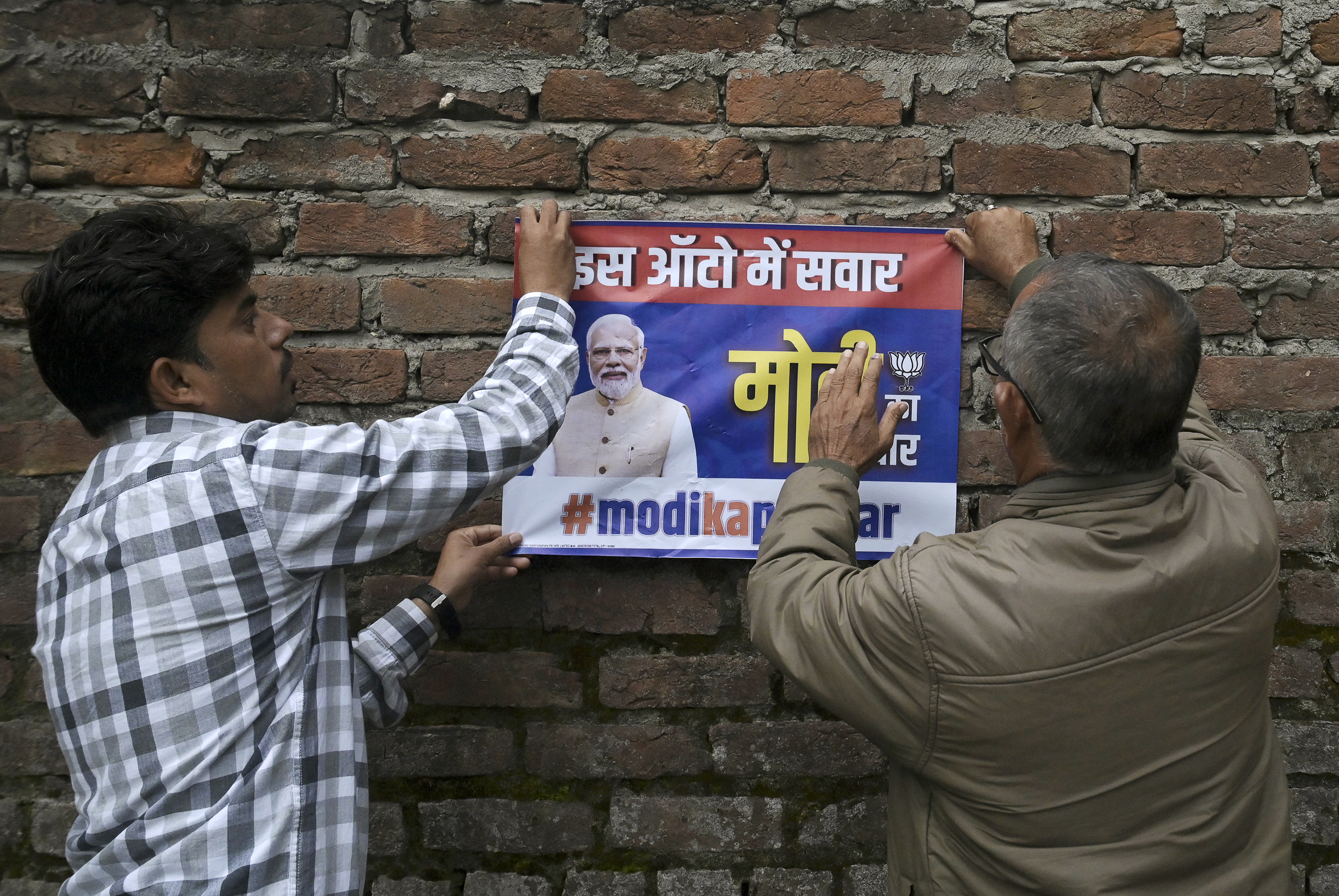 Activistas del Partido Bhartiya Janta (BJP) pegan un cartel con la imagen del líder del BJP y primer ministro indio, Narendra Modi, en una pared cerca de un colegio electoral durante la primera fase de votación de las elecciones generales de la India en Jammu, a unos 230 kilómetros de Srinagar, el 19 de abril. , 2024.