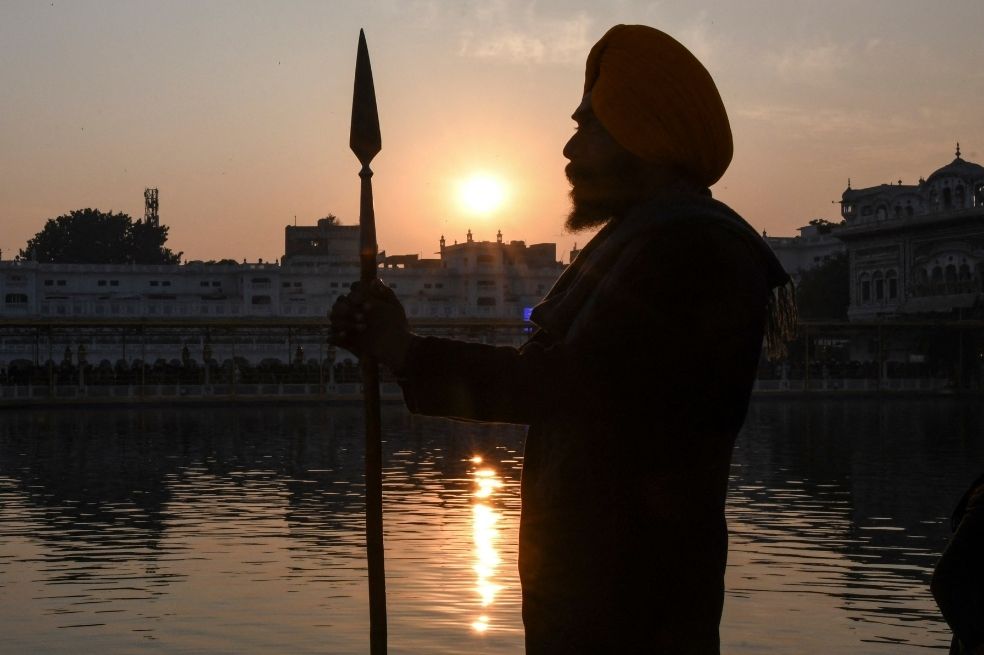 Un voluntario sij hace guardia durante la última puesta de sol de 2021 en la víspera del Año Nuevo 2022, en el Templo Dorado del santuario sij en Amritsar, Singapur.