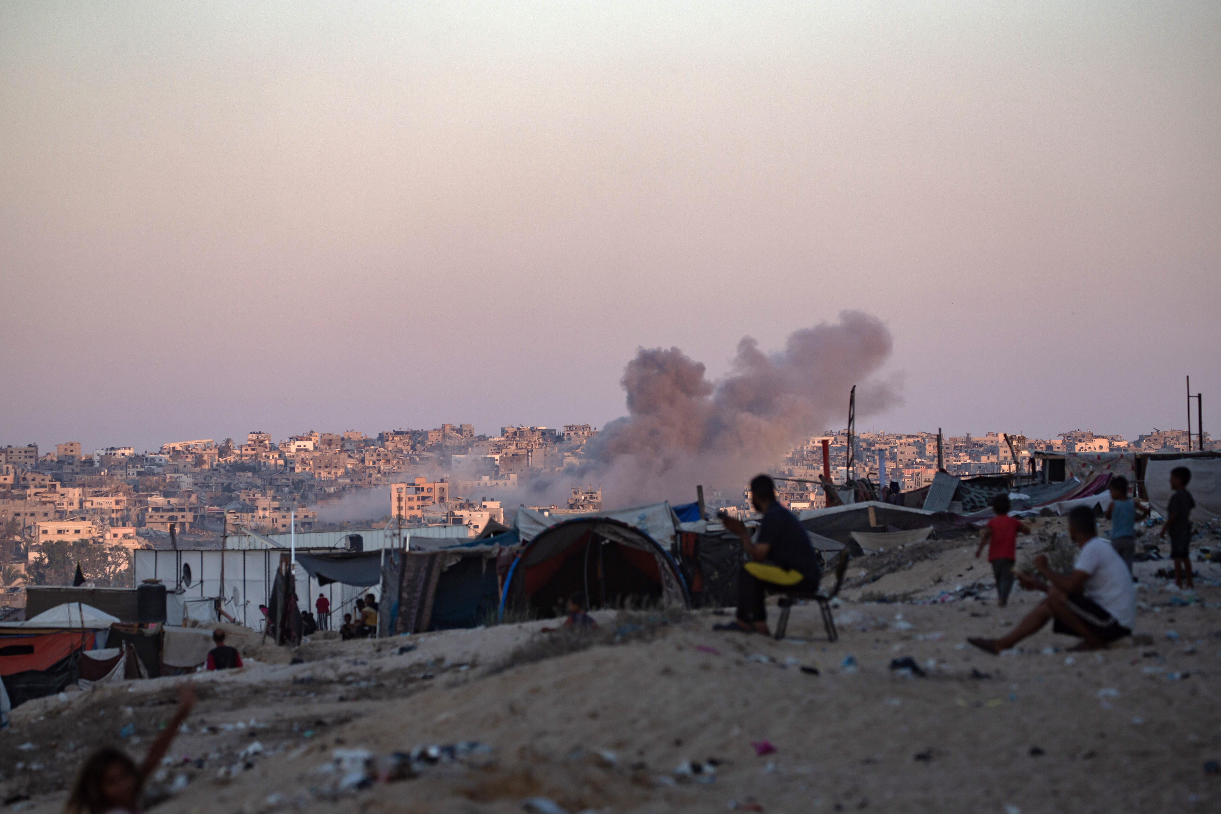 Gaza (--), 13/08/2024.- Smoke rises following an Israeli air strike as internally displaced Palestinians sit next to their tents in Khan Younis camp, southern Gaza Strip, 13 August 2024. More than 39,900 Palestinians and over 1,400 Israelis have been killed, according to the Palestinian Health Ministry and the Israel Defense Forces (IDF), since Hamas militants launched an attack against Israel from the Gaza Strip on 07 October 2023, and the Israeli operations in Gaza and the West Bank which followed it. EFE/EPA/HAITHAM IMAD