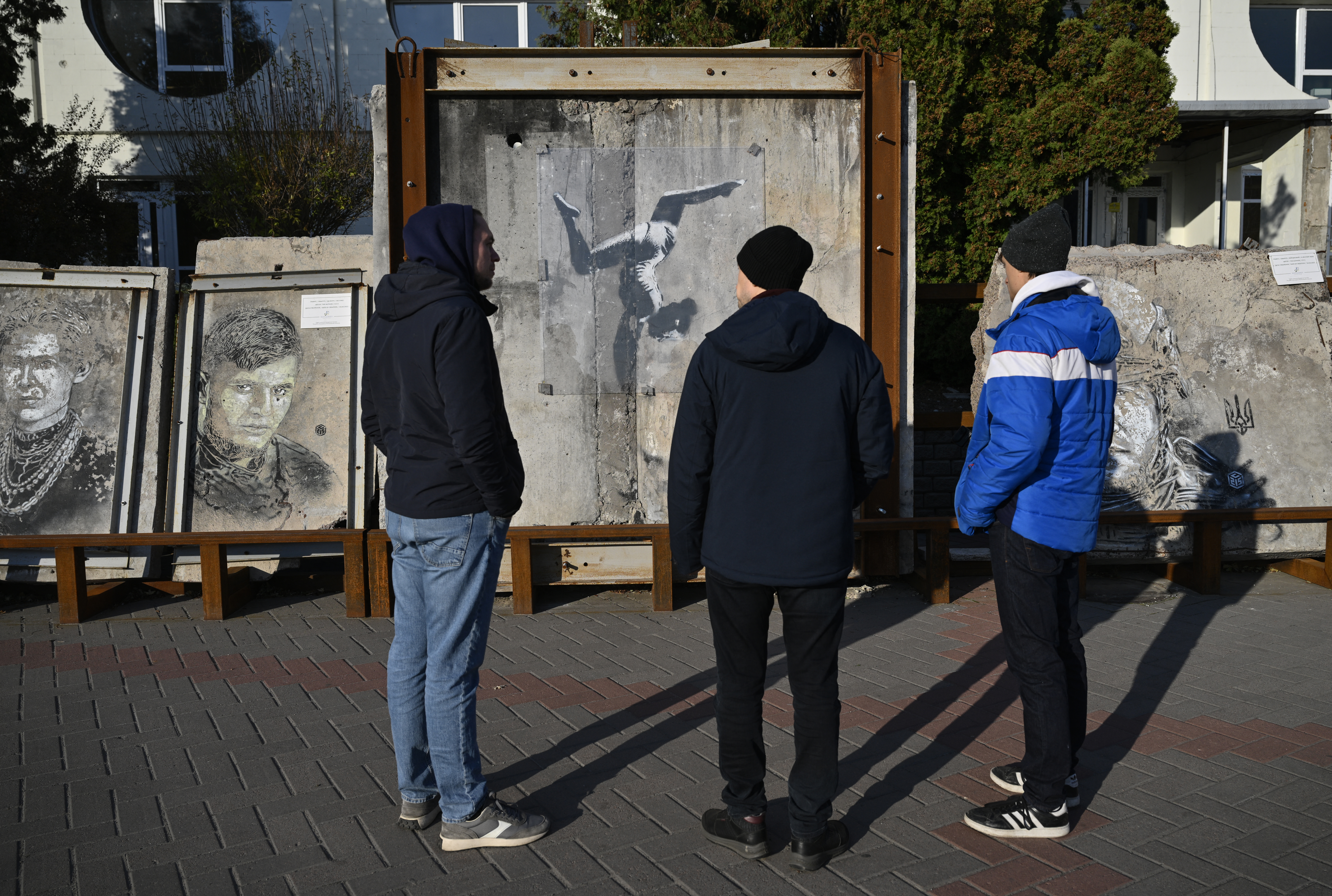Spanish traveller Alberto Blasco Ventas (R), tour guide Oleksiy Goryachev (L) and co-founder of War Tours Dmytro Nykyforov look at a creation by England-based street artist Banksy during a tour at an open air exhibition of graffiti created by International and Ukrainian artists which were painted on the ruins of destroyed buildings in Borodyanka, Kyiv region, on November 7, 2024, amid the Russian invasion of Ukraine.
