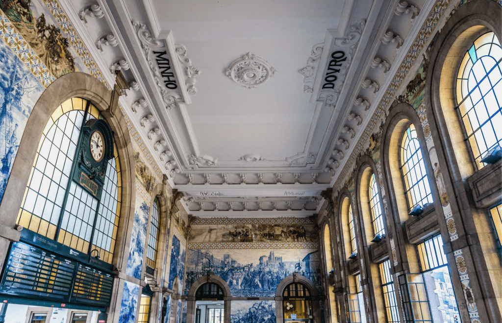 La Estação de São Bento, inaugurada en 1916, es una de las estaciones más bellas del país y un símbolo de Oporto. Diseñada por el arquitecto José Marques da Silva en estilo Beaux-Arts, destaca por su impresionante vestíbulo revestido con más de 20.000 azulejos creados por Jorge Colaço, que narran episodios clave de la historia de Portugal en tonos azul y blanco. Ubicada en pleno centro histórico, no solo funciona como estación, sino también como una galería viva que mezcla arte, memoria y vida cotidiana.