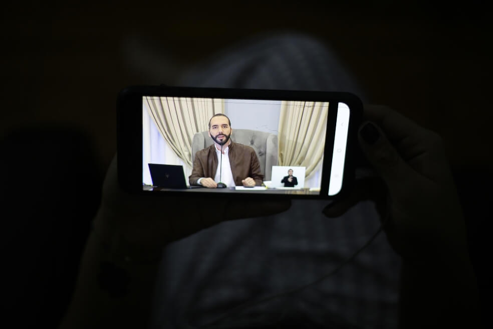 Una joven sintoniza desde su teléfono móvil la cadena de televisión donde el presidente de El Salvador, Nayib Bukele, cuenta los avances en la lucha contra el coronavirus.  / EFE