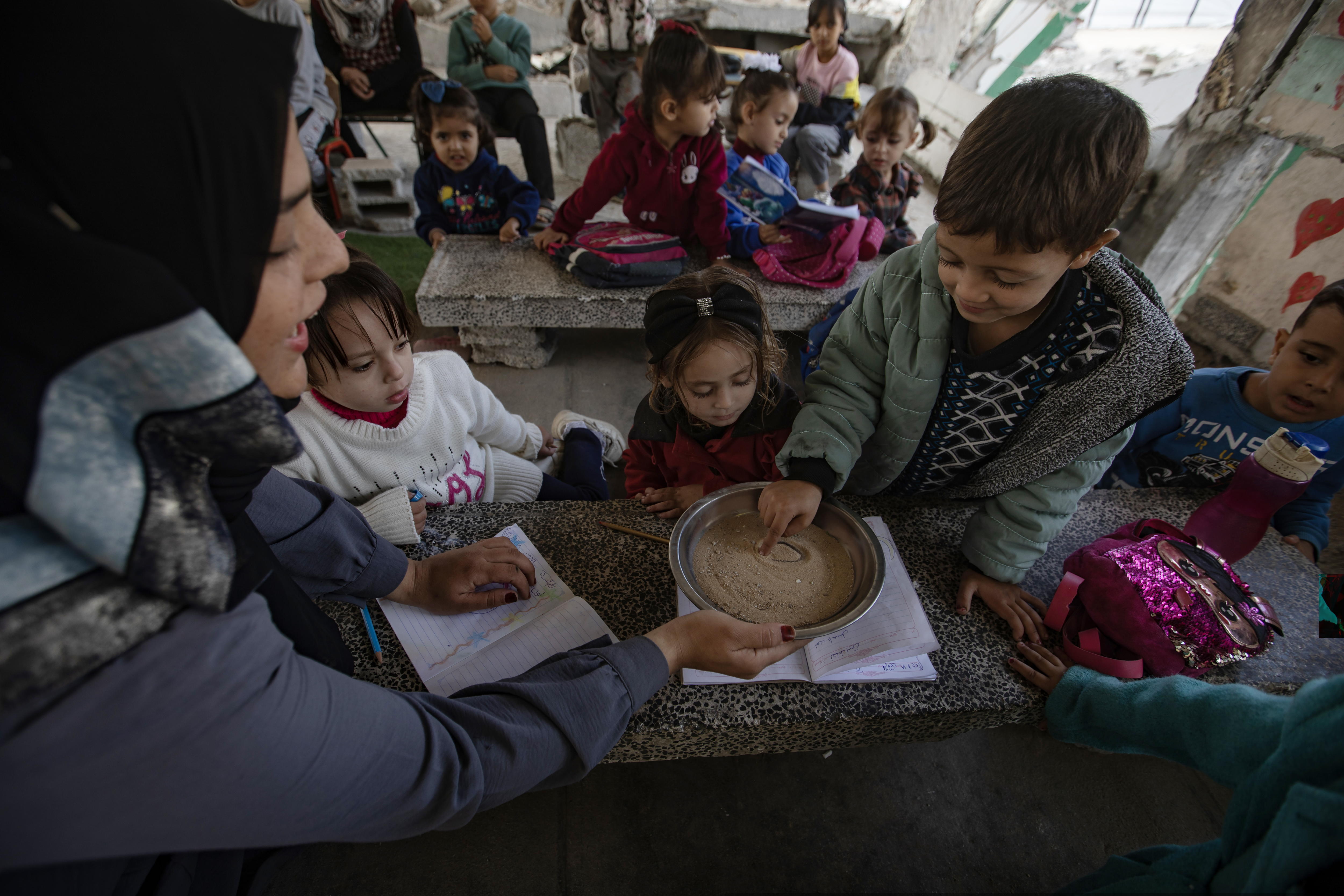 FOTODELDÍA Khan Younis (Gaza), 18/11/2024. - Un niño palestino escribe en una bandeja de arena en un aula sobre los escombros de una escuela destruida en el campamento de Khan Younis, al sur de la Franja de Gaza, este lunes. Según el Ministerio de Salud palestino, más de 43.800 palestinos han sido asesinados desde que los militantes de Hamas lanzaron un ataque contra Israel desde la Franja de Gaza el 7 de octubre de 2023, y el 44 por ciento del total eran niños, según el ACNUDH. EFE/ Haitham Imad