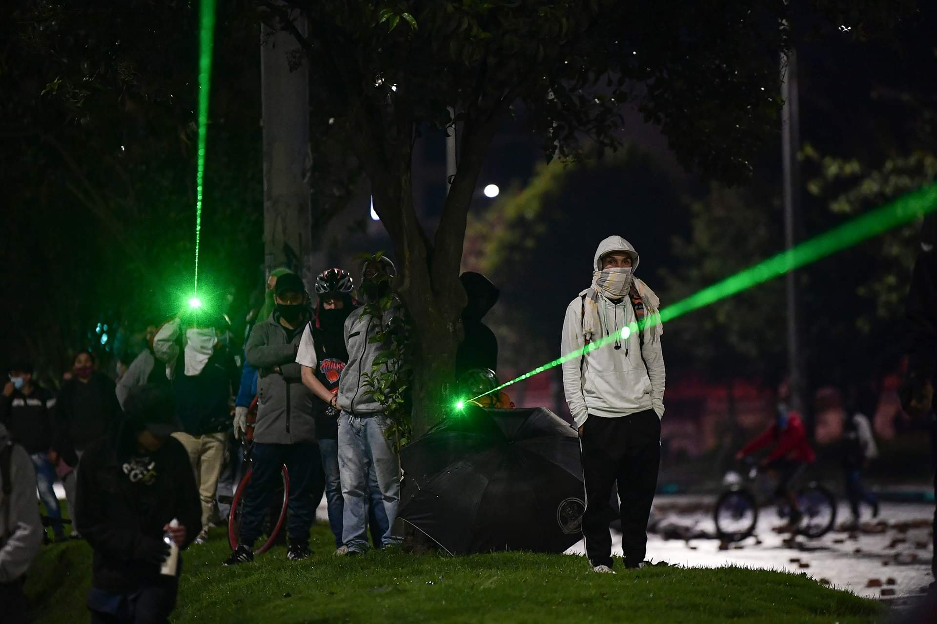 Varios hombres junto a un árbol. Dos de ellos apuntan con láser verde