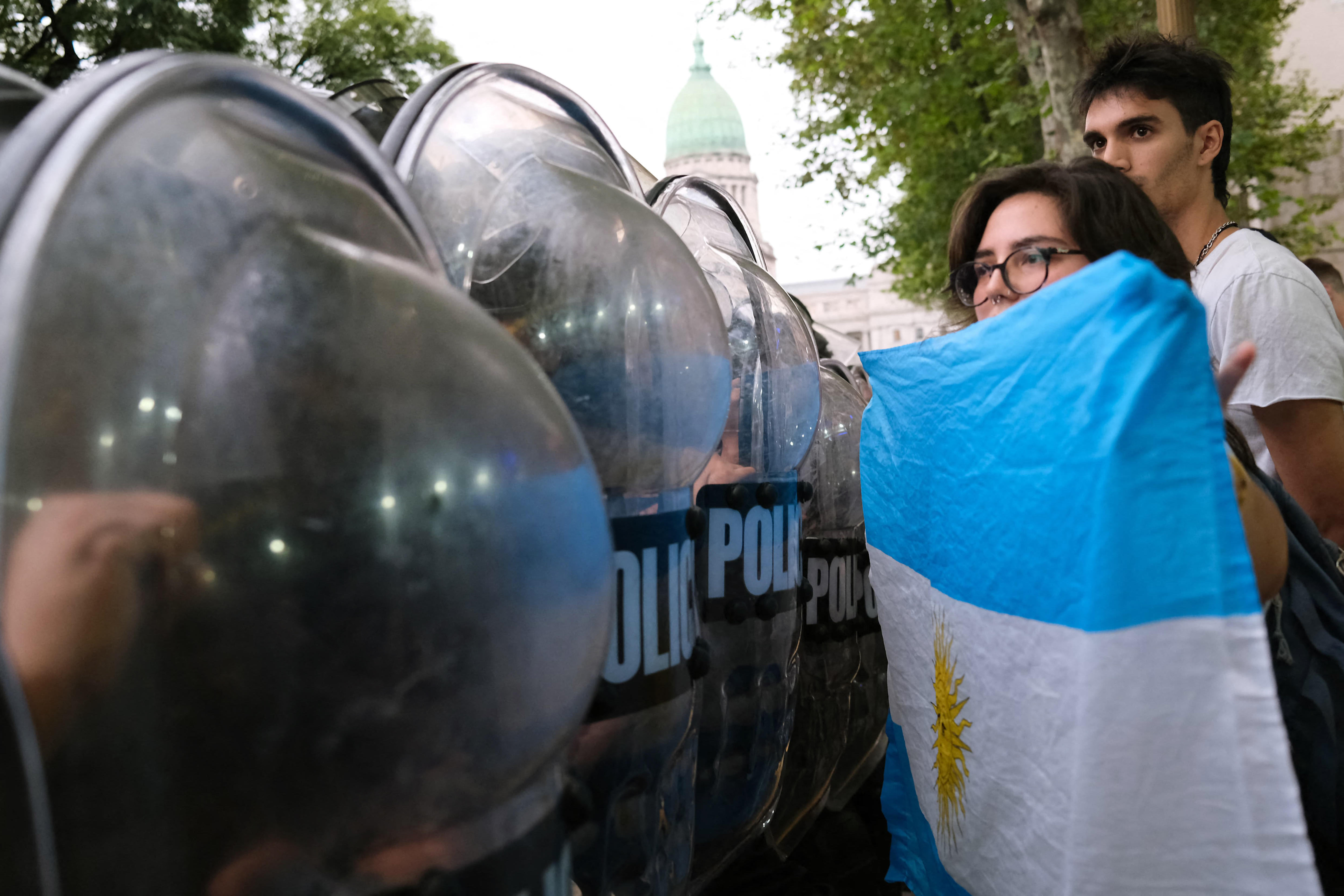 A woman holds an Argentine flag in front of a police cordon during a protest against Javier Milei's government cutbacks on the film institute funding, at the time the ultra-liberal "Decree of Necessity and Urgency" (DNU) is being debated, outside of the Gaumont cinema in front of the Congress in Buenos Aires, on March 14, 2024. Senators started to debate the so-called DNU, a mega-decree that modifies or repeals hundreds of rules and laws and is part of the president's plan to deregulate and disestablish Argentina's economic system as much as possible. (Photo by Ignacio SANCHEZ MELLO / AFP)