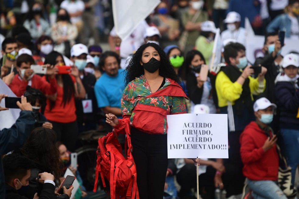 una mujer desfila con prendas realizadas por excombatientes de las farc y con u letrero en el que pide la implementación del acuerdo de paz