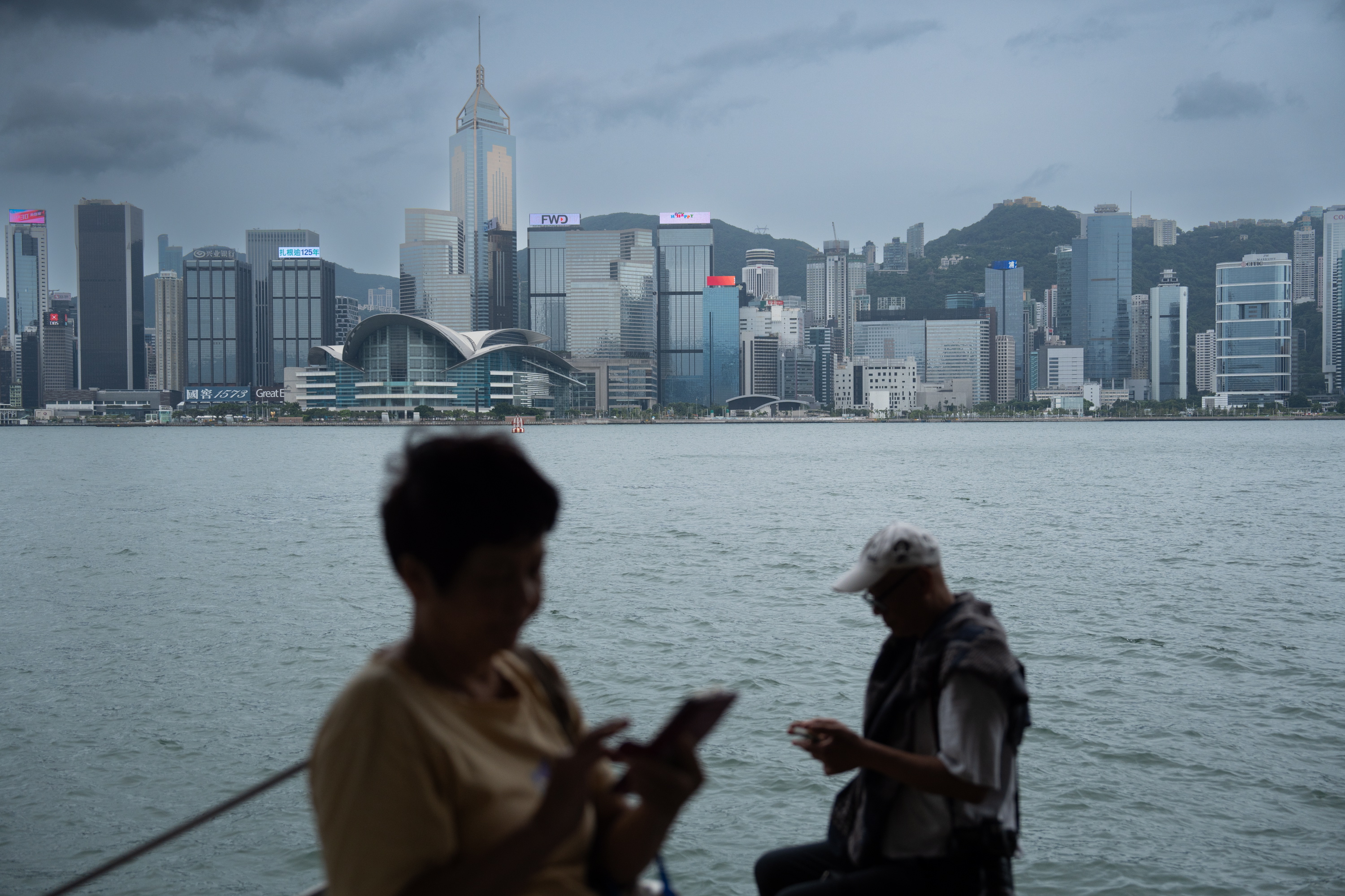 Hong Kong (China), 01/09/2023.- People check their phones in front of the Hong Kong island skyline during Typhoon Saola, in Hong Kong, China, 01 September 2023. The No.8 typhoon warning was raised on the morning of 01 September as Typhoon Saola arrived in Hong Kong. The stock market was closed and schools suspended in the city in response to the typhoon. EFE/EPA/Bertha Wang