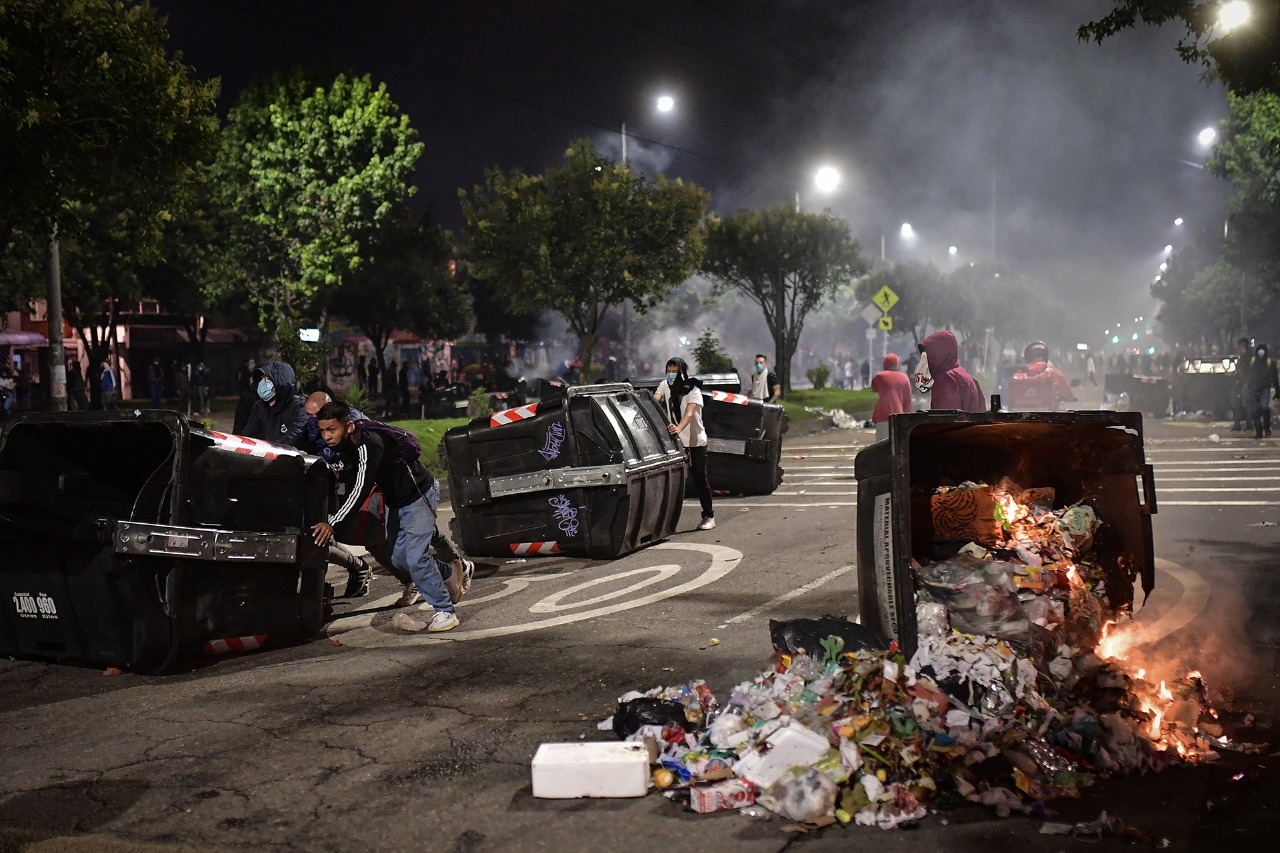 Varias personas corriendo contenedores de basura sobre la vía.