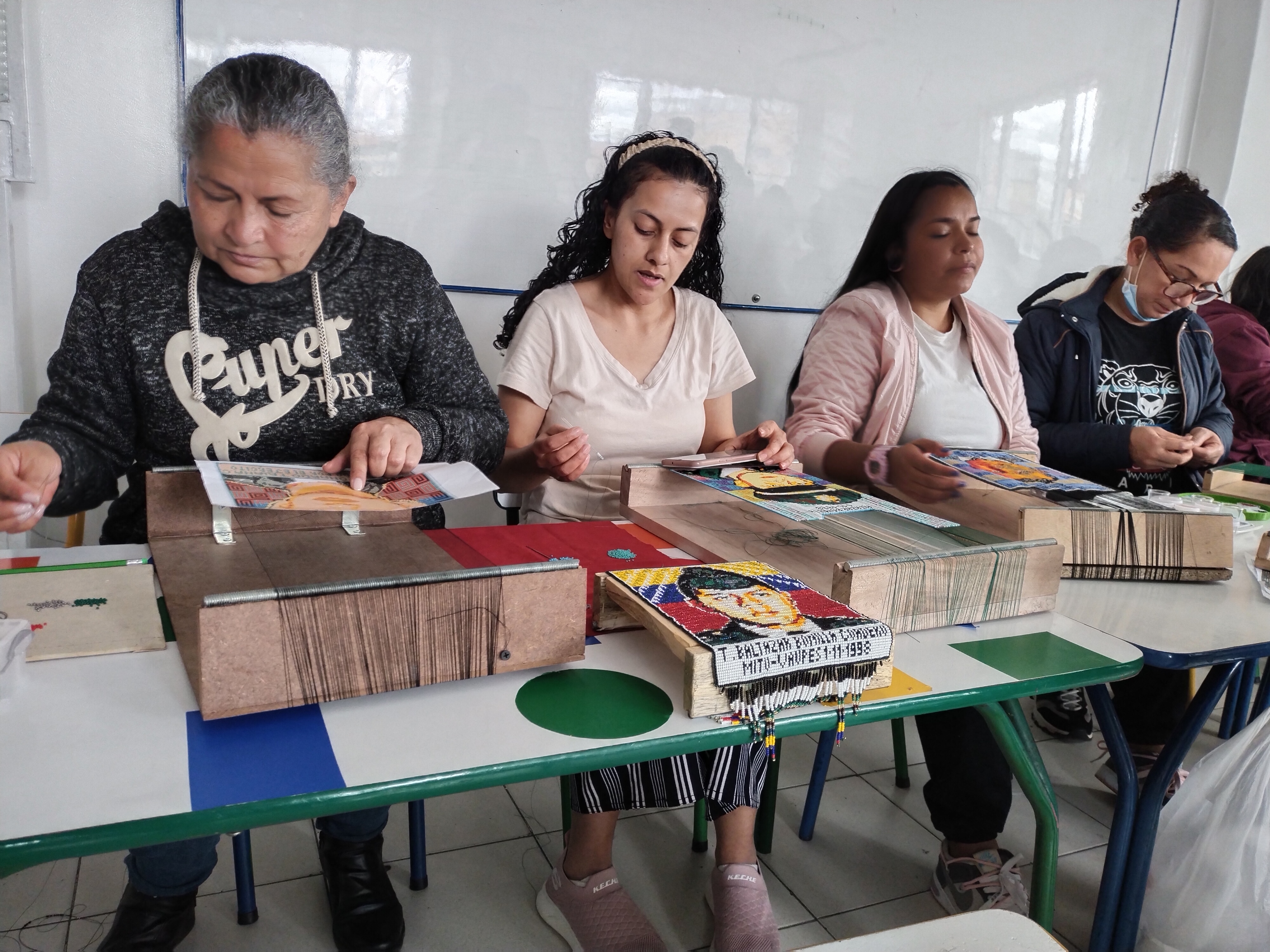 Cuatro mujeres tejen figuras sobre una mesa rectangular