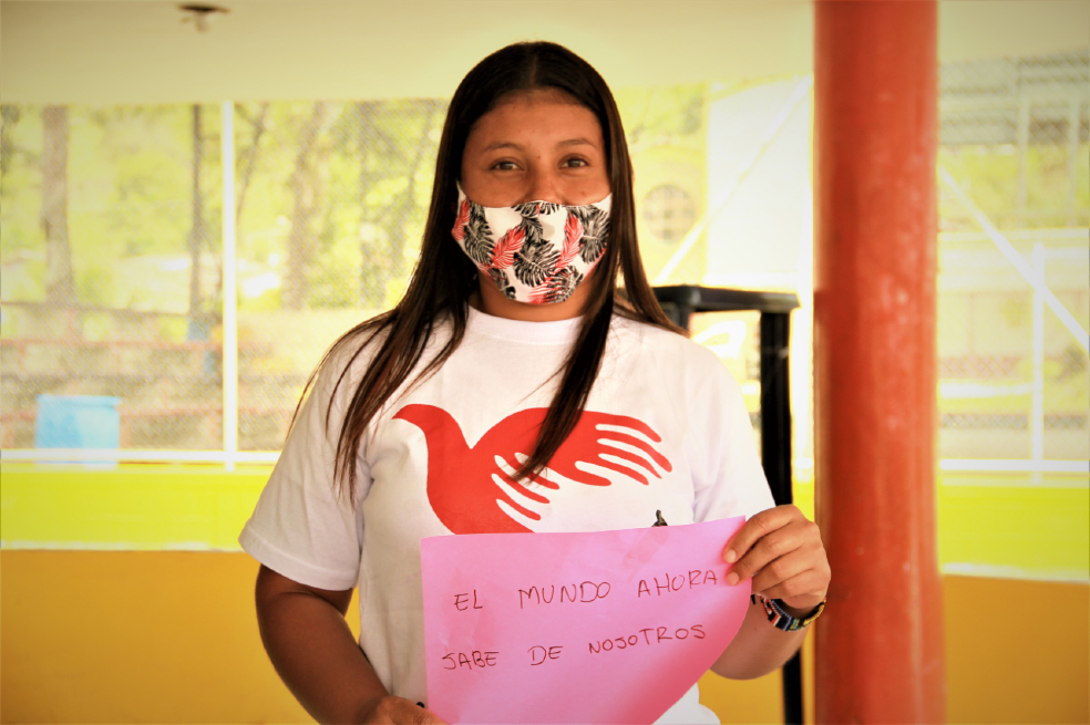 Una jóven sostiene una pancarta que tiene un mensaje de paz.