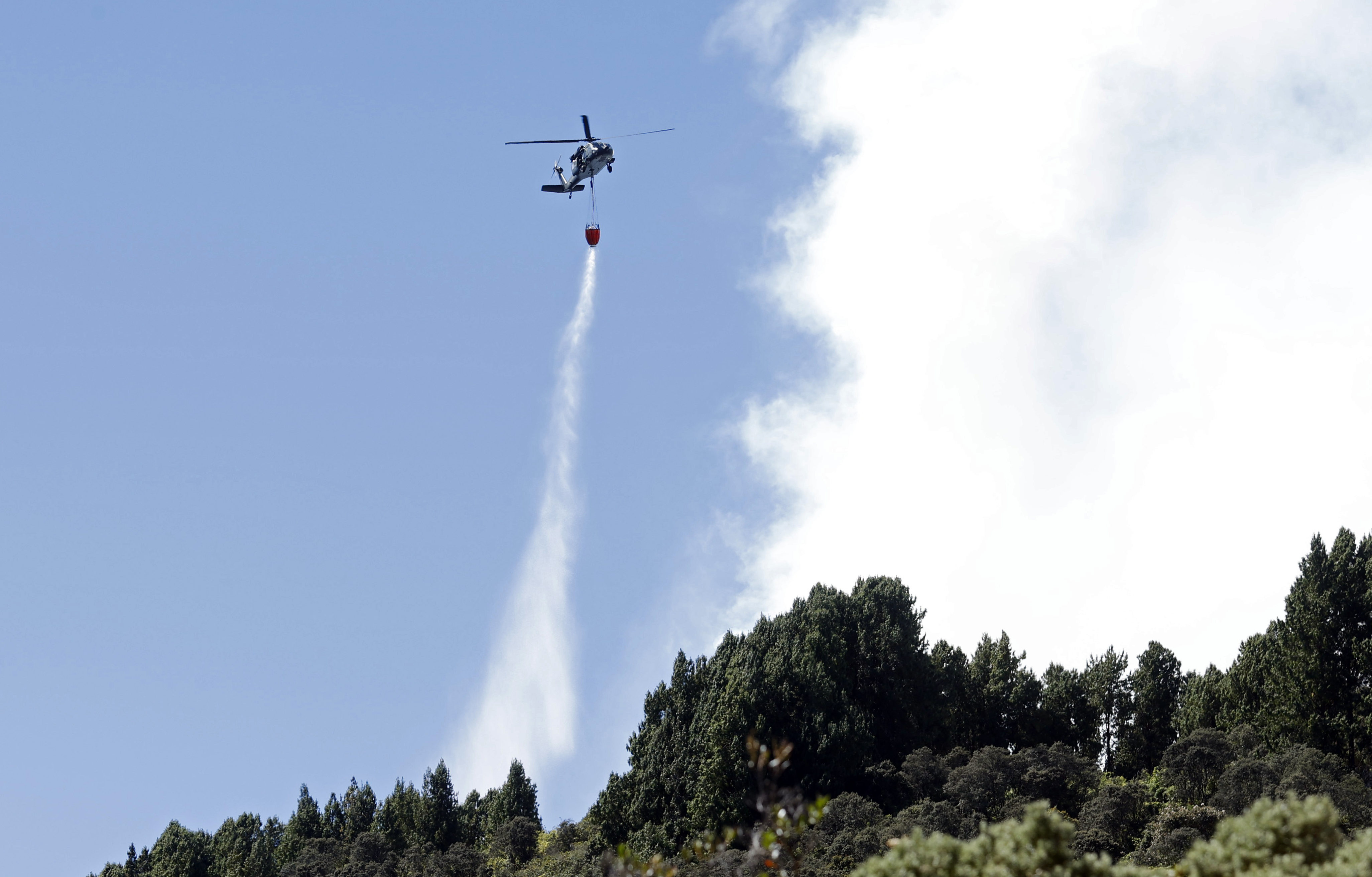 AME2250. BOGOTÁ (COLOMBIA), 25/01/2024.- Fotografía de un helicóptero mientras hace una descarga de agua en la zona de un incendio forestal hoy, en el cerro El Cable, en Bogotá (Colombia). Un total de 31 incendios forestales están activos este jueves en Colombia y afectan a nueve departamentos y Bogotá, donde sigue la emergencia por los fuegos en dos de sus cerros, informó este jueves la Unidad de Nacional de Gestión del Riesgo de Desastre (Ungrd). Los más preocupantes son precisamente los de los cerros orientales y El Cable de Bogotá, pues el humo se extiende por buena parte de la capital y está afectando la calidad del aire y las operaciones aéreas. EFE/ Mauricio Dueñas Castañeda