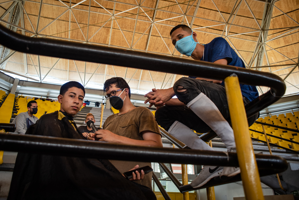 Jefferson Hernández, 23 años, barbero, corta el pelo a sus compañeros para pasar el tiempo en uno de los centros de cuarentena establecidos por las autoridades venezolanas para los migrantes que regresan al estado fronterizo de Táchira. Jefferson caminó durante dos meses desde Perú a Venezuela para volver a casa en medio de una pandemia que lo dejó sin trabajo. Está en cuarentena con su esposa y su hijo de 18 meses.